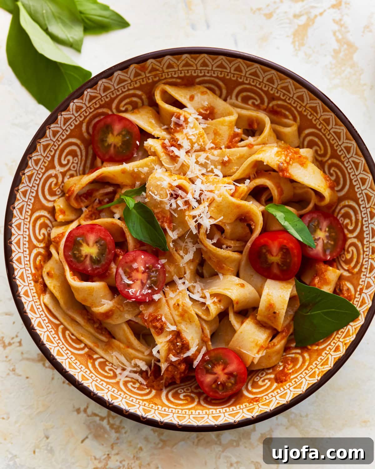 A bowl of almond flour pasta with fresh vegetables, shredded cheese, and herbs