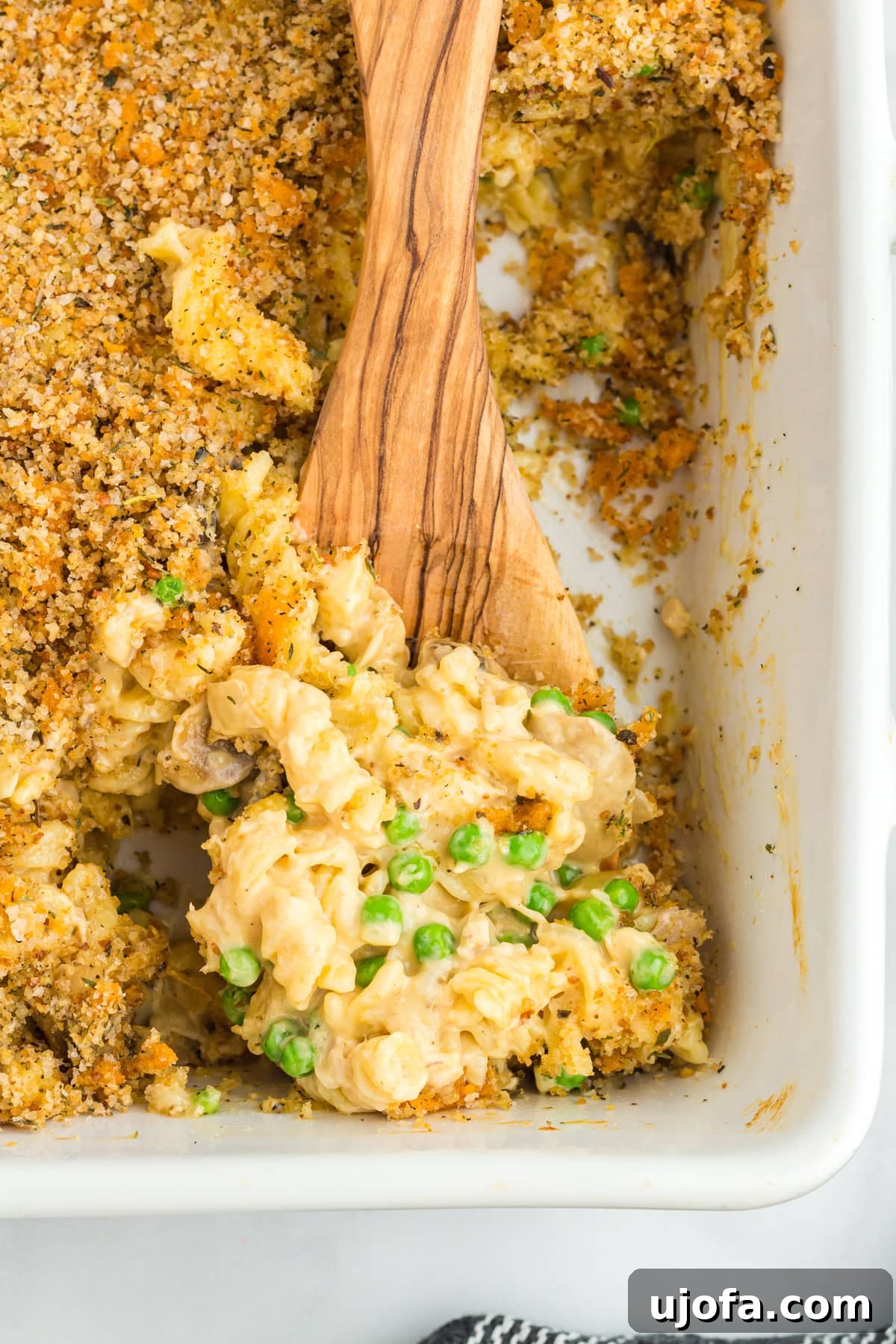 A wooden spoon scooping gluten-free tuna casserole from the baking dish