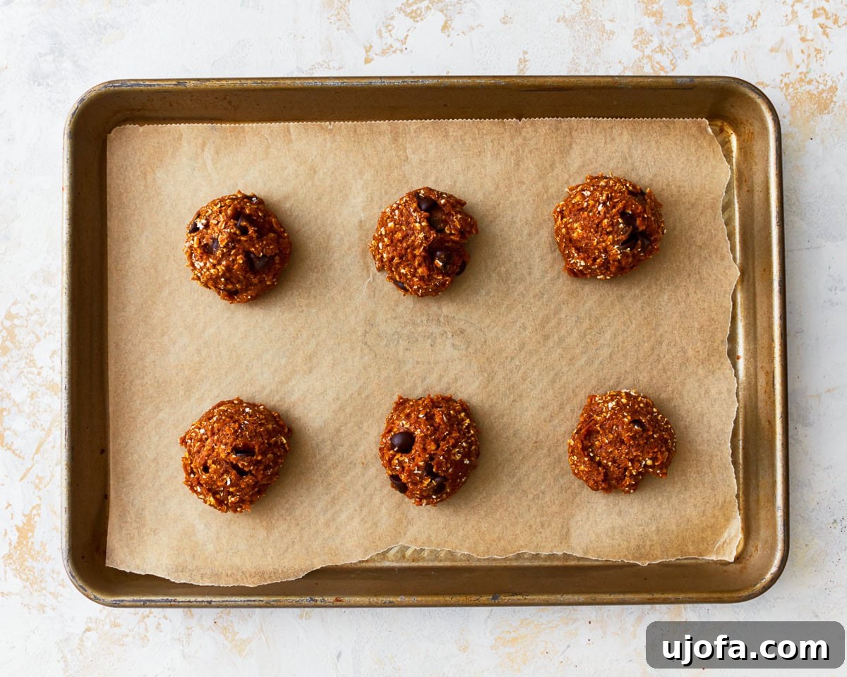 Scoops of gluten-free peanut butter oatmeal cookie dough on a parchment lined baking sheet, spaced for baking.