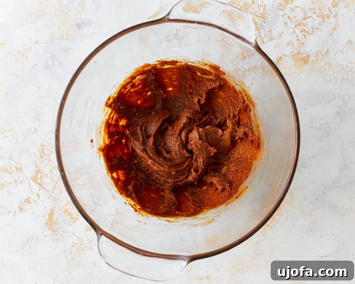 Brown sugar and egg base for gluten-free peanut butter oatmeal cookies in a mixing bowl, illustrating the addition of eggs.