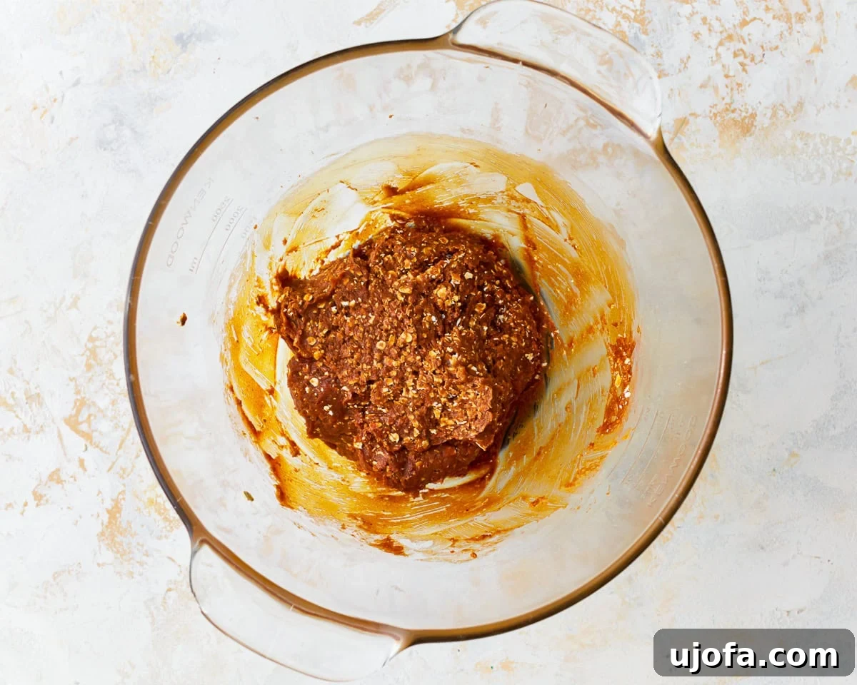 Gluten-free peanut butter oatmeal cookie dough in a glass mixing bowl, showing the texture after oats and leavening agents are added.