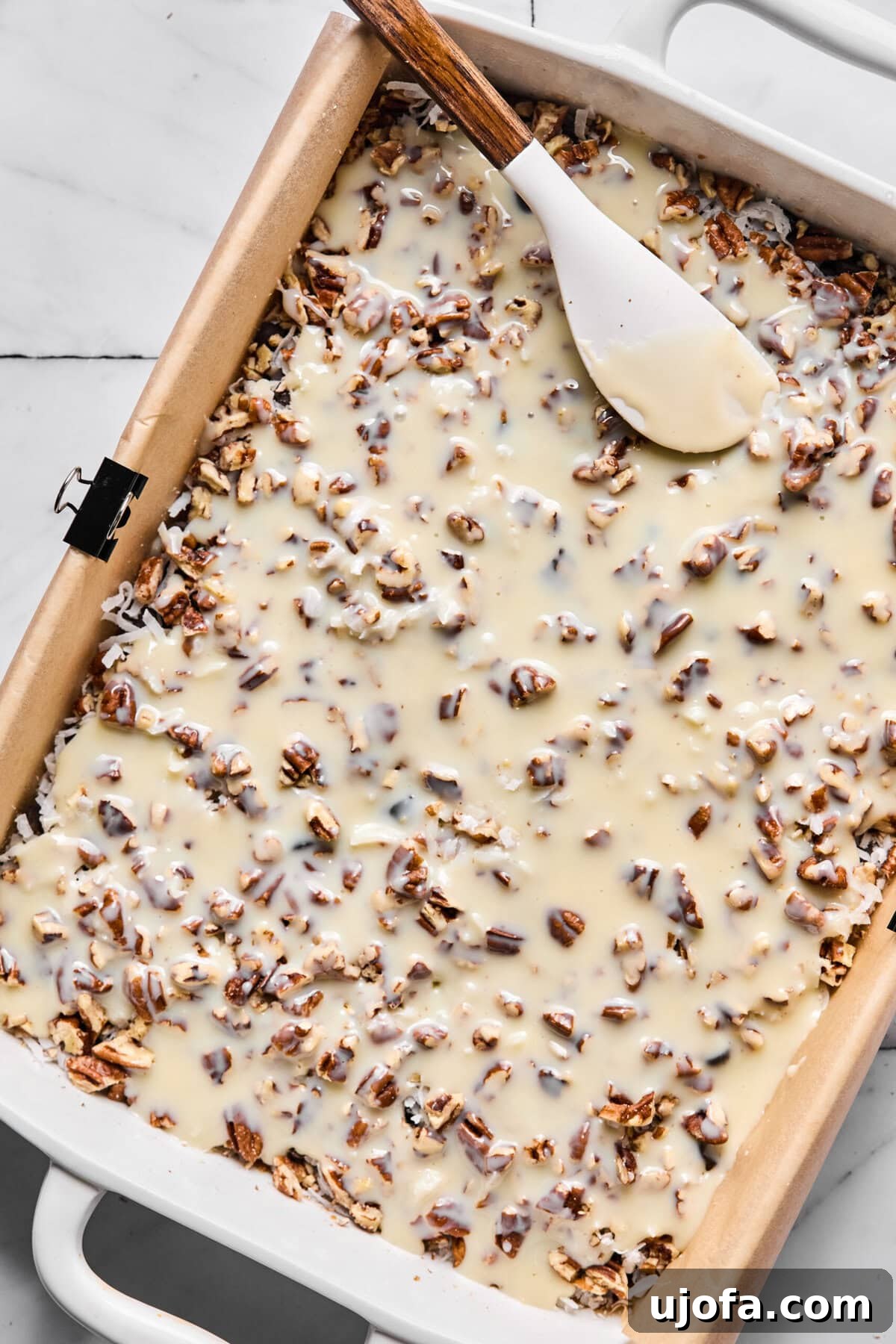 Wondrously Easy Allergen Friendly Bars 8 Sweetened condensed milk poured evenly over layered ingredients, preparing for baking.