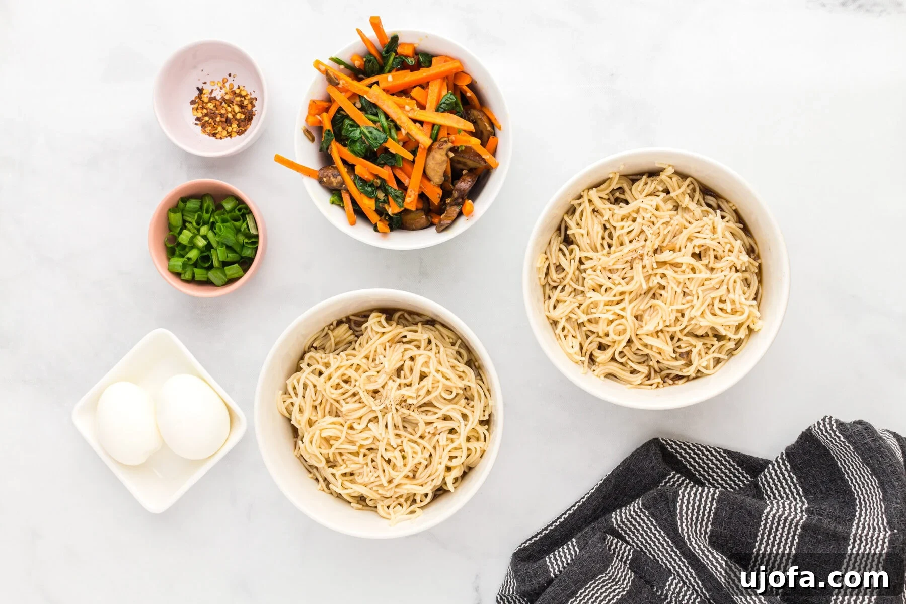 Gluten-free ramen noodles in bowls, surrounded by separate bowls of sautéed vegetables, green onions, and crushed red pepper flakes.