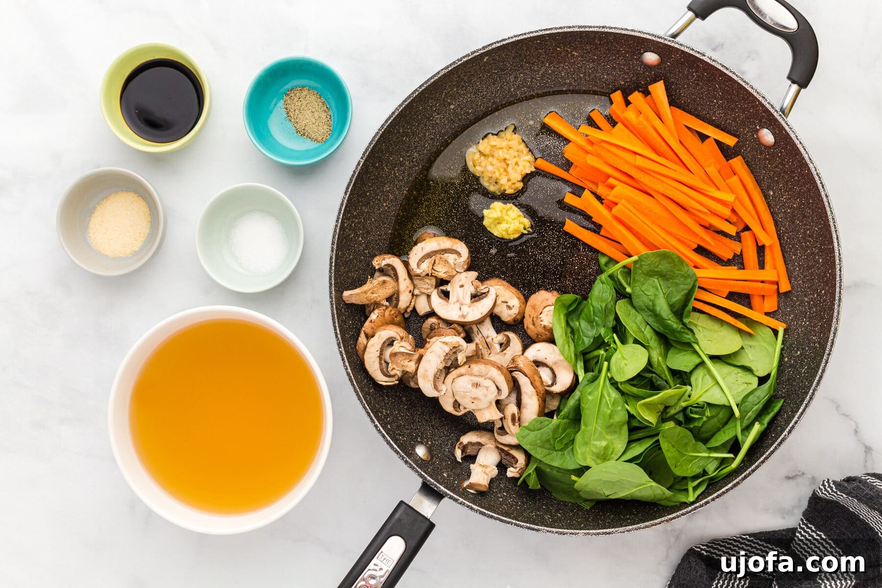 Sliced carrots, baby spinach, and mushrooms ready to be sautéed in a skillet with garlic and ginger.
