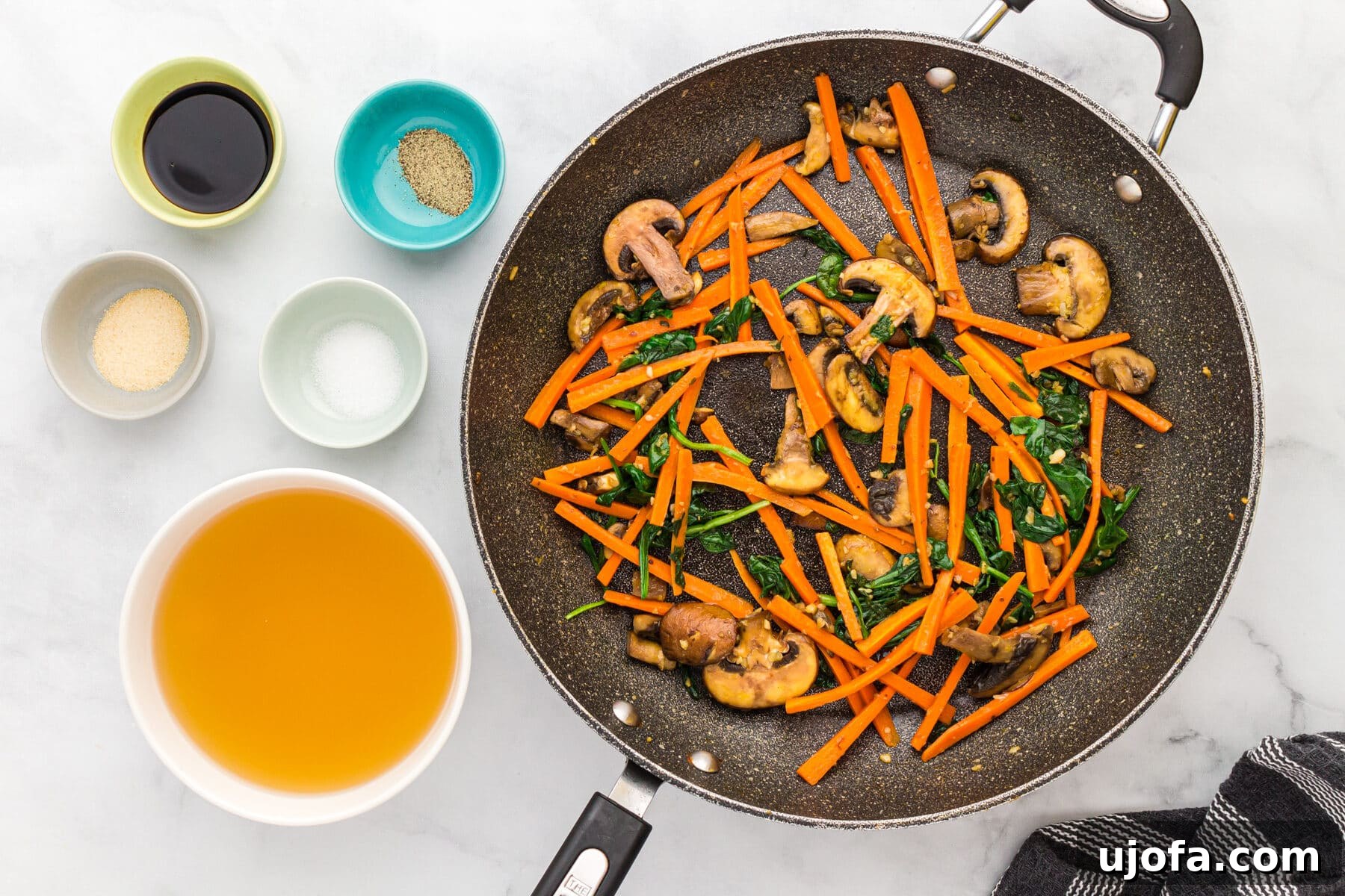 Sautéed carrots, mushrooms, and spinach in a skillet, softened and ready to be removed.