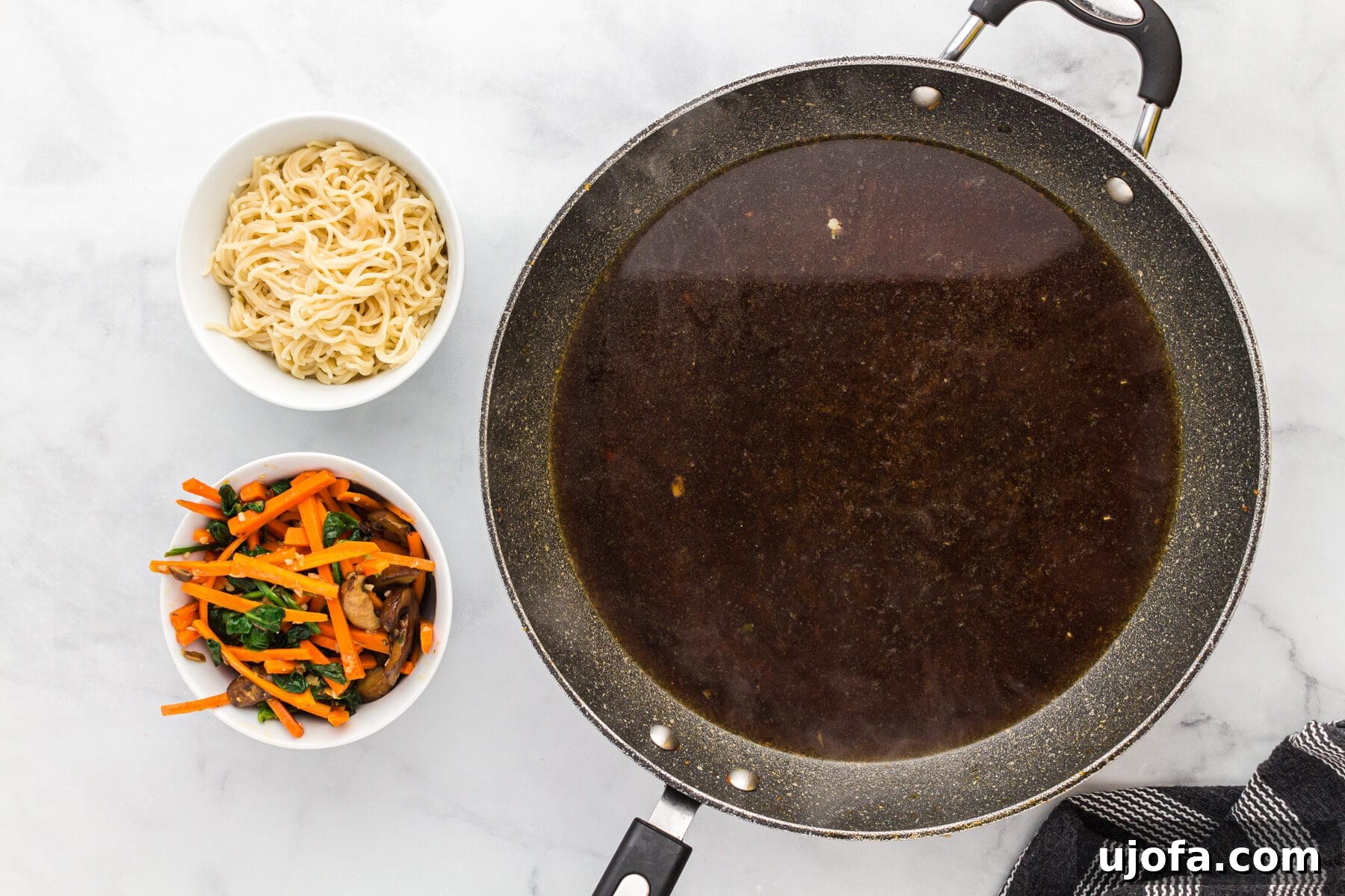 Chicken broth simmering in a skillet, with a bowl of sautéed vegetables and gluten-free ramen noodles nearby.