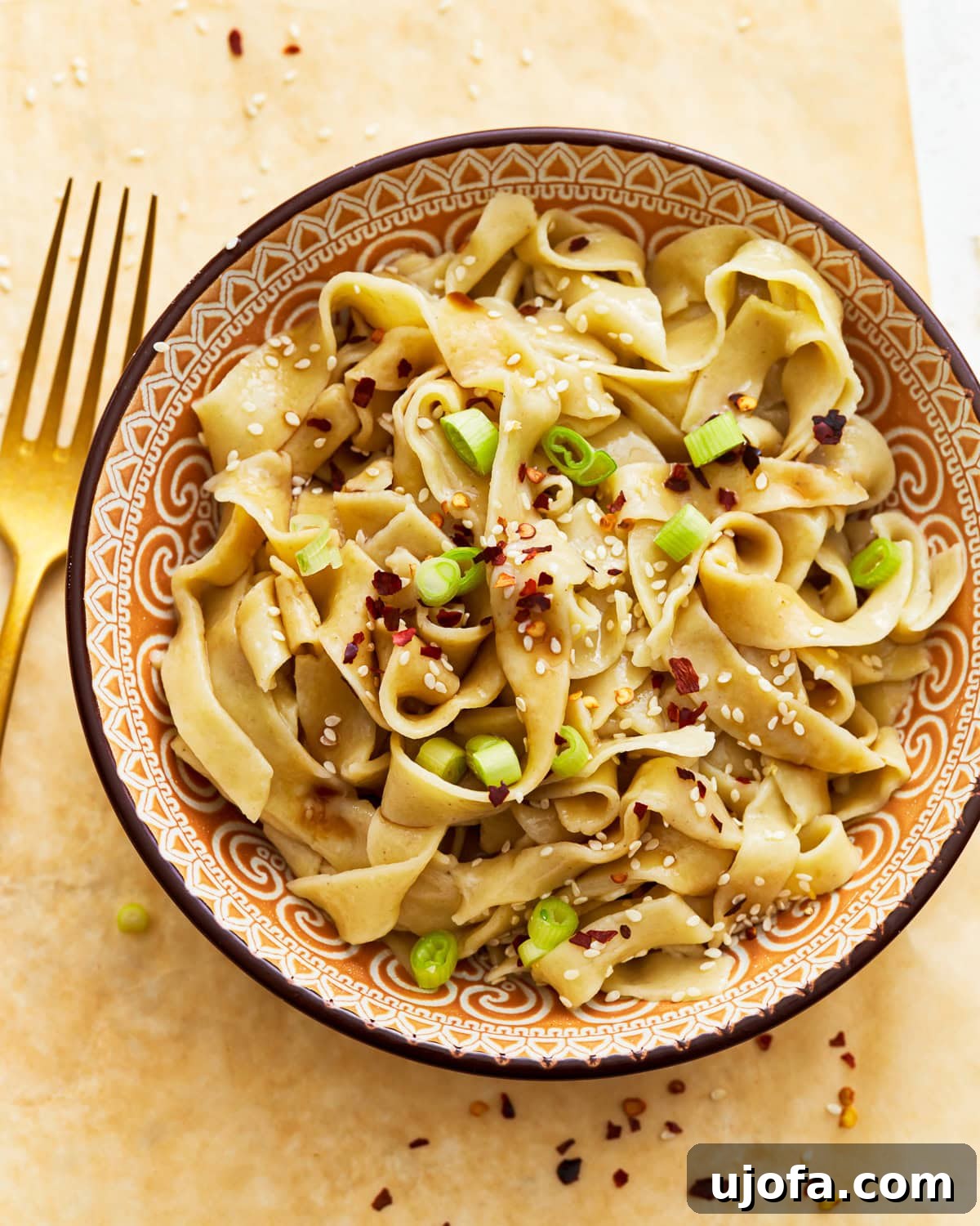 Gluten-free egg noodles in a bowl with vibrant green onions, sesame seeds, and a sprinkle of red pepper flakes, ready to be enjoyed.