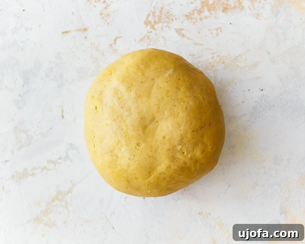 A smooth, elastic ball of gluten-free egg noodle dough resting on a lightly floured surface after being kneaded.