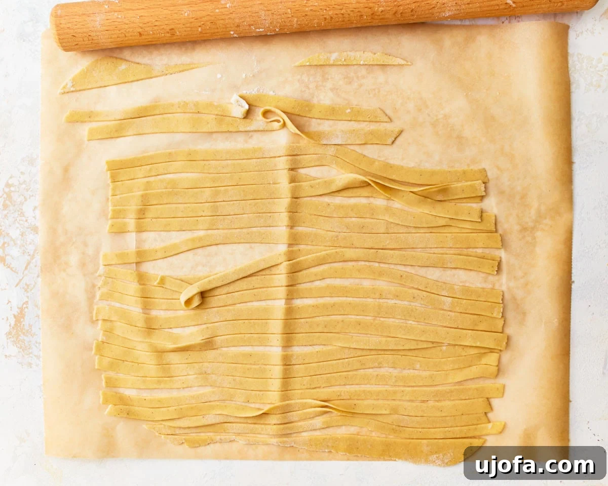 Thinly rolled gluten-free egg noodle dough cut into uniform strips on parchment paper, ready for cooking.