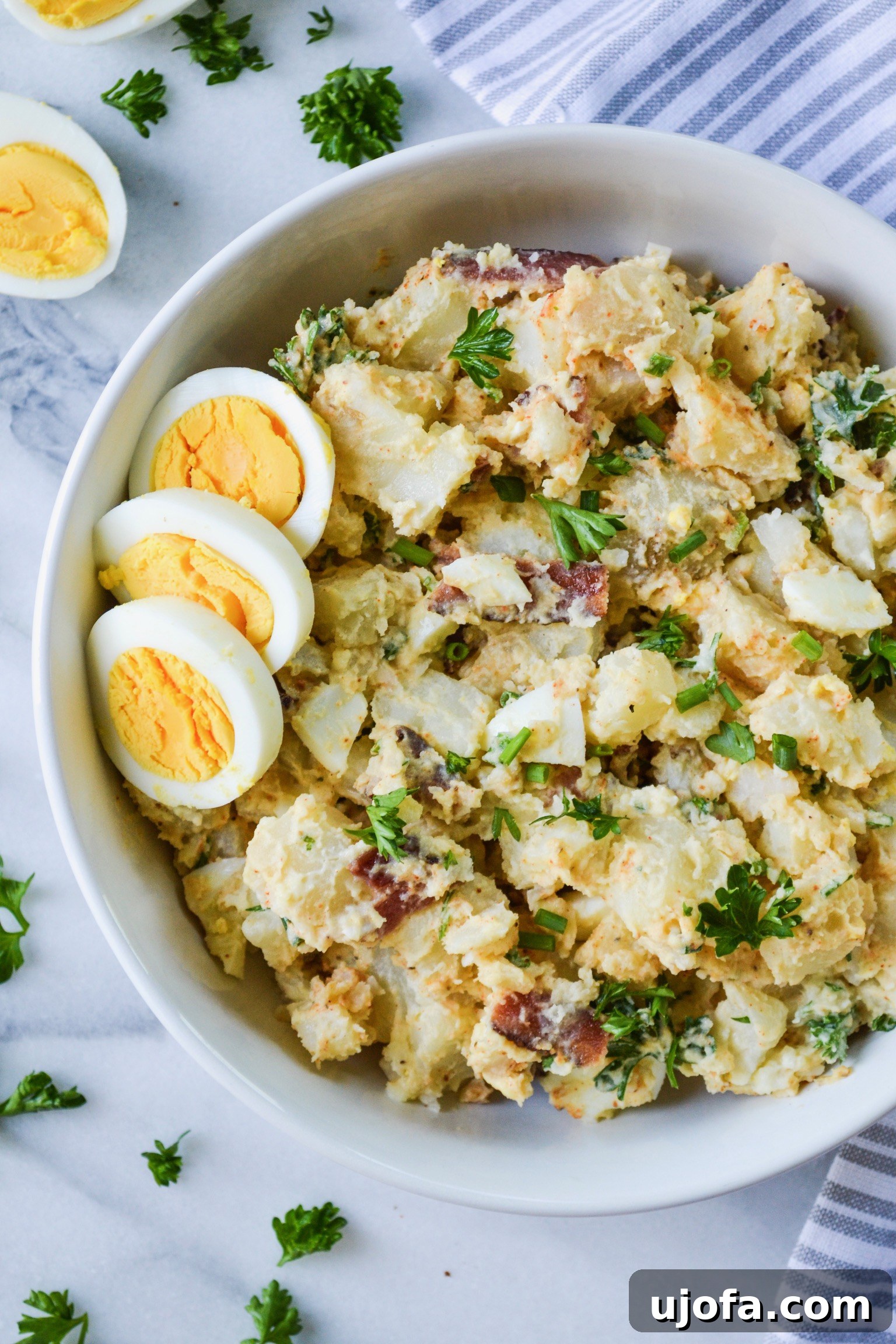 Creamy Whole30 Deviled Egg Potato Salad in a white bowl, garnished with paprika and fresh chives.