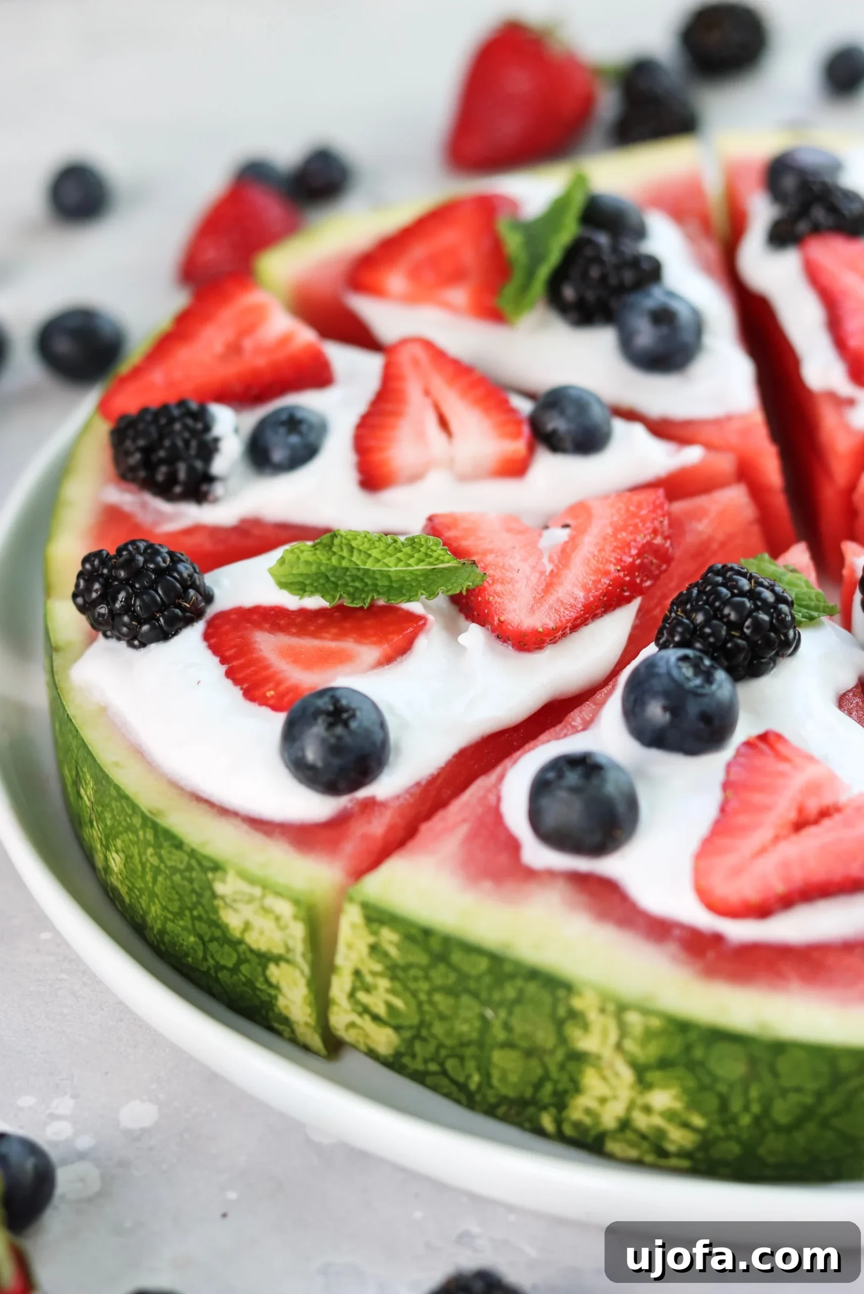 Colorful Whole30 Watermelon Pizza topped with coconut cream, fresh berries, and mint leaves, cut into slices.