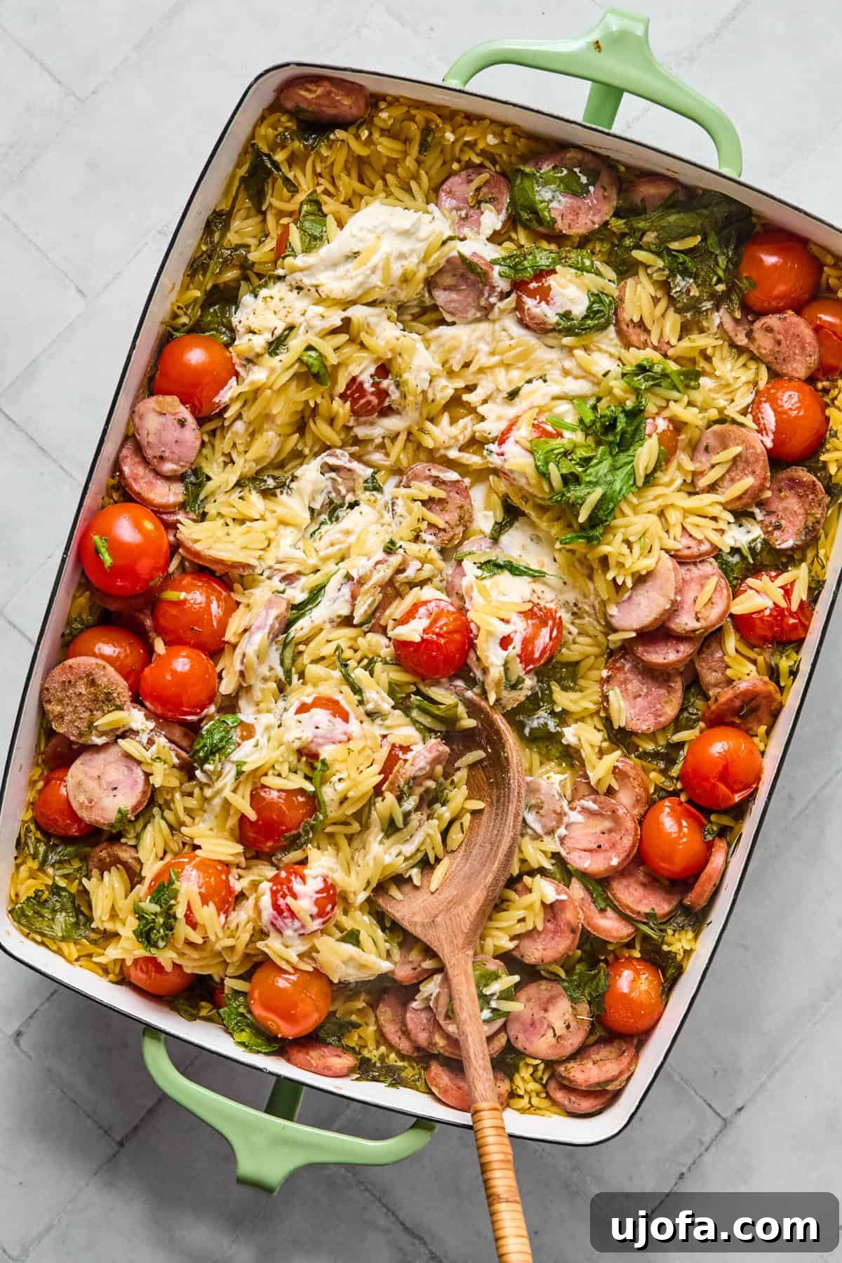 Kremamsı Boursin Orzo Tavuk Sosisli Tek Tencere Keyfi 7 One pan orzo bake fresh out of the oven, with a spoon stirring the melted Boursin and cooked ingredients to form a creamy sauce.