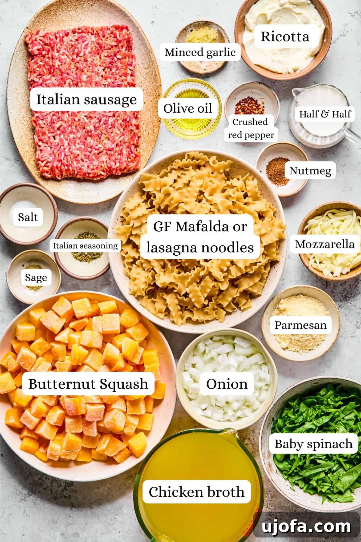 Comforting Butternut Squash Lasagna Soup 3 Various ingredients for butternut squash lasagna soup, including Italian sausage, diced onion, minced garlic, cubed butternut squash, fresh spinach, gluten-free pasta, and assorted cheeses, neatly arranged on a white kitchen surface.