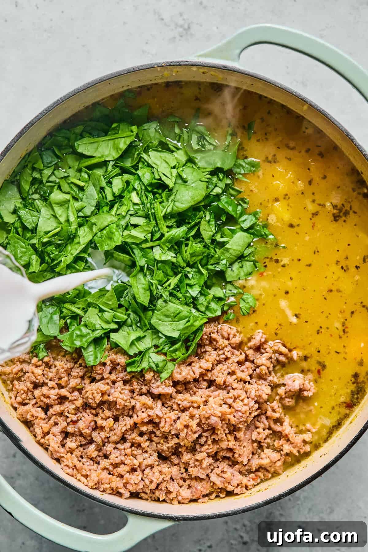 Comforting Butternut Squash Lasagna Soup 8 The browned Italian sausage, fresh spinach, and half-and-half being stirred back into the creamy butternut squash lasagna soup mixture in a large pot.