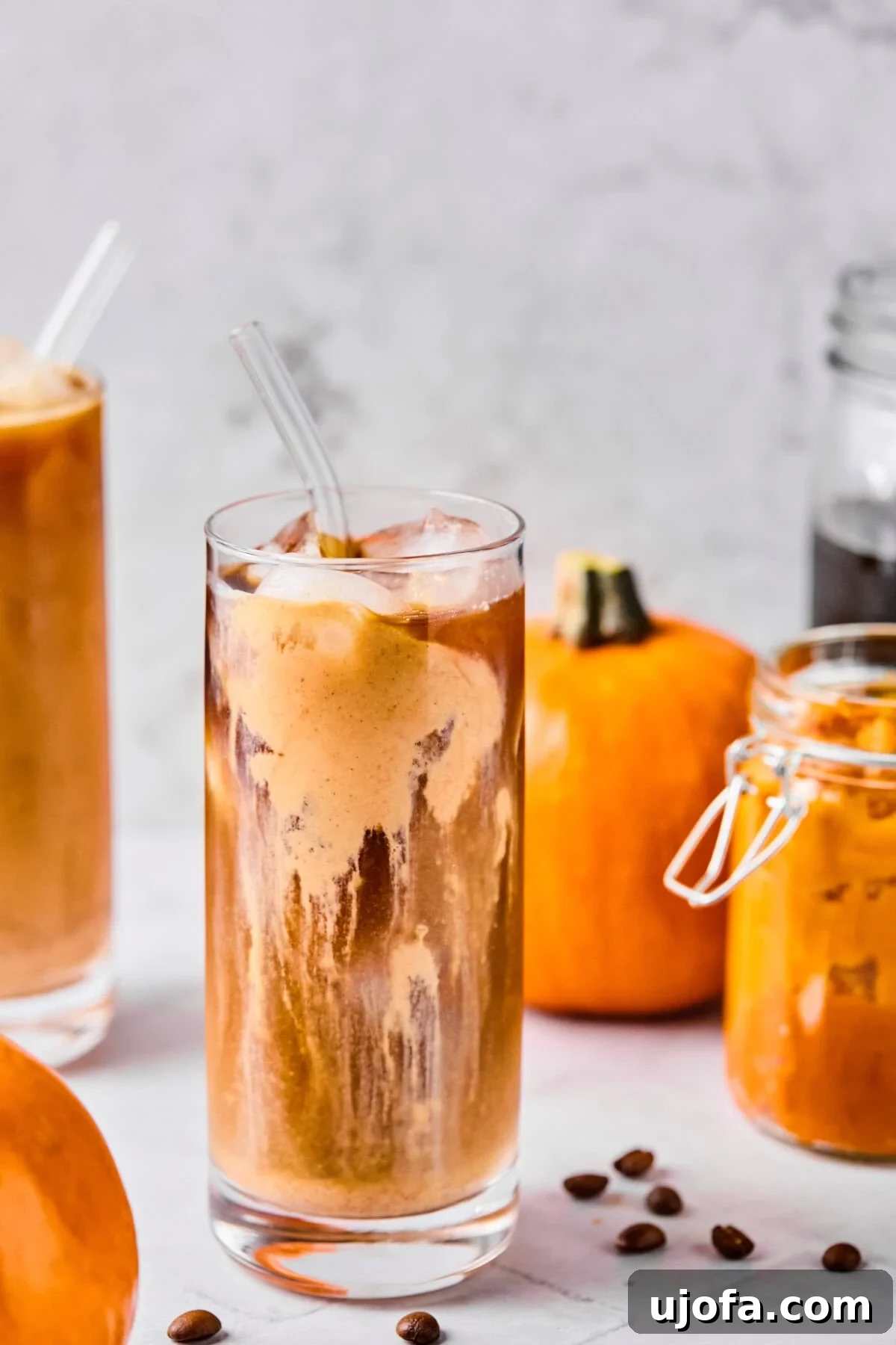 A glass of cold brew coffee topped generously with a creamy, orange-hued pumpkin protein cold foam, artfully arranged with miniature pumpkins and autumn foliage in the background, evoking a cozy fall atmosphere.