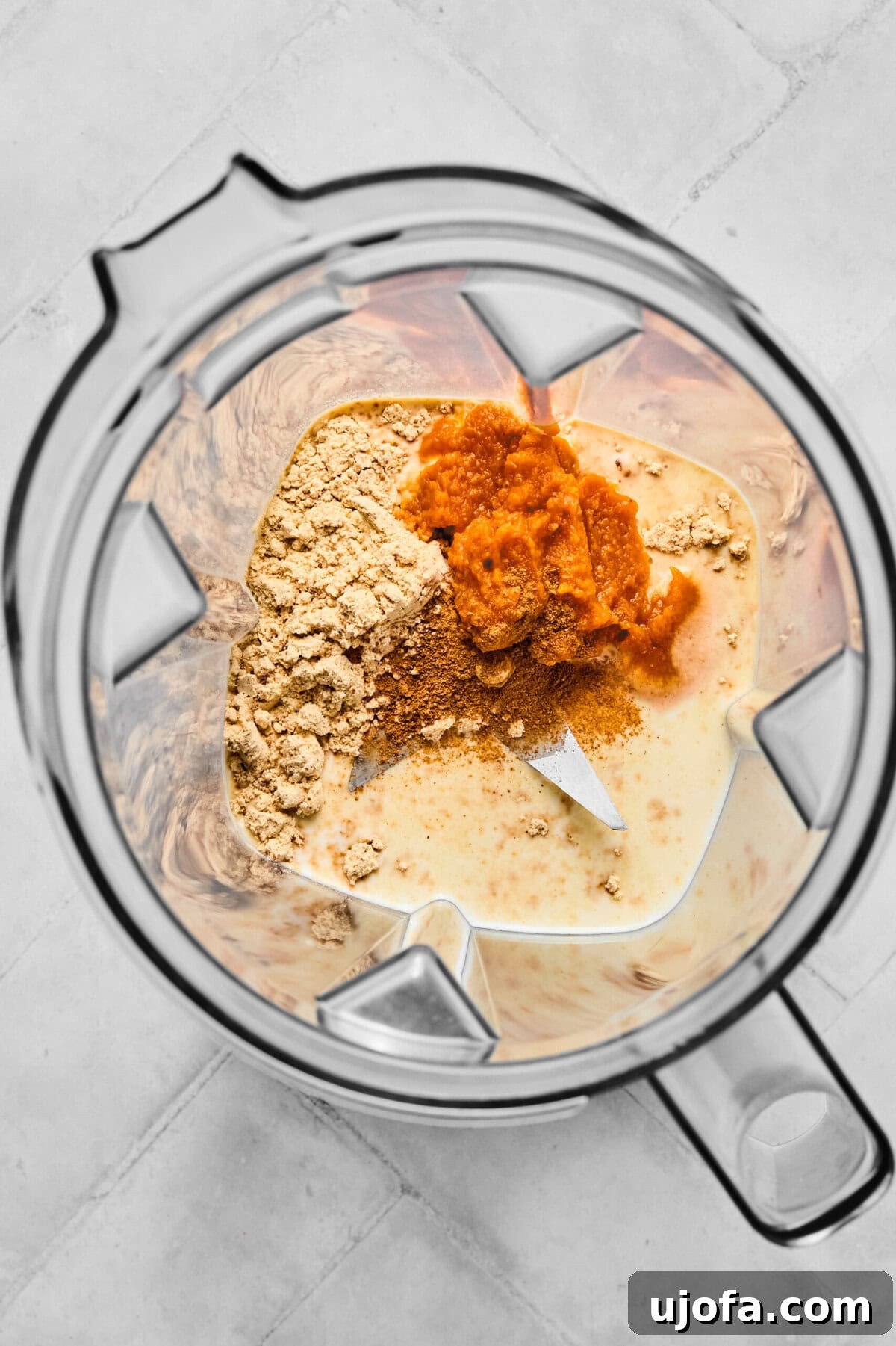 All the ingredients for pumpkin cold foam, including protein powder, pumpkin puree, pumpkin pie spice, and half and half, carefully placed inside a small blender or frother cup, ready for blending.