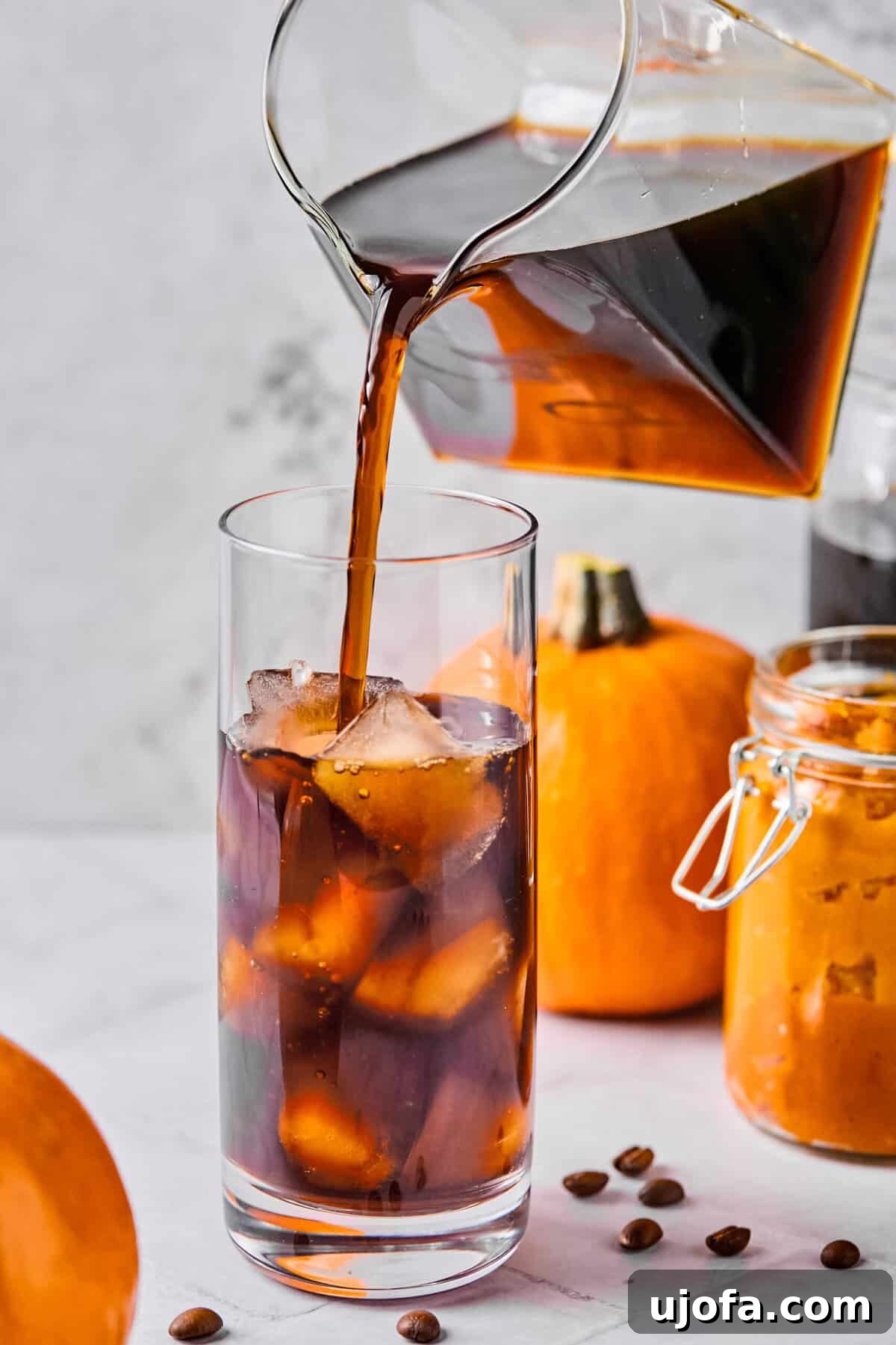 A glass filled with ice cubes, with cold brew coffee being poured over them, creating a rich, dark base for the cold foam to be added later.