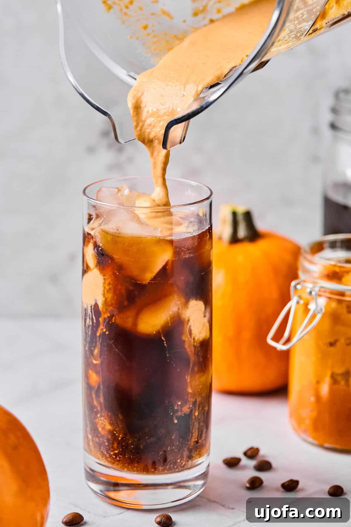 The creamy pumpkin protein cold foam being gently spooned or poured onto the surface of the cold brew coffee in a glass filled with ice, creating distinct, beautiful layers.