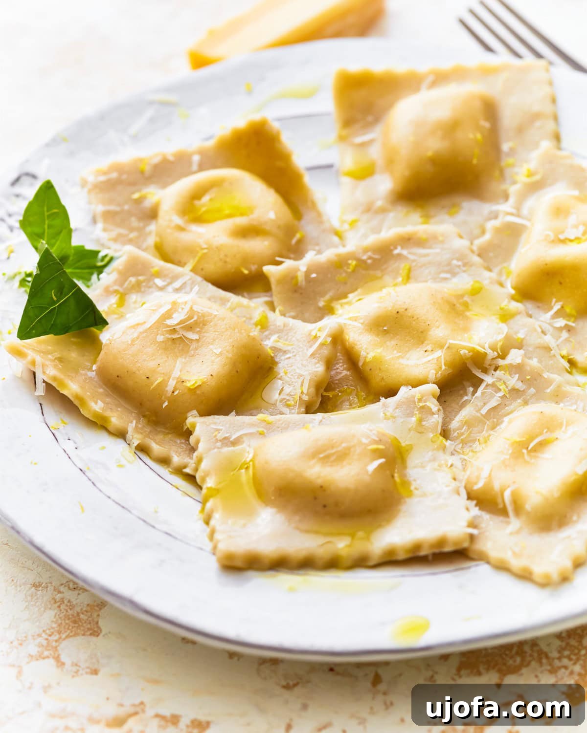 Side view of gluten-free ravioli on a plate with fresh herbs, olive oil, and shredded cheese.