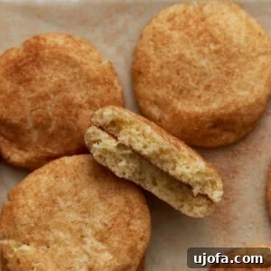 Soft gluten-free snickerdoodle cookies arranged on parchment paper, with one cookie broken in half to reveal its fluffy, tender interior and cinnamon sugar coating.