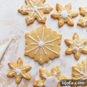 Beautifully decorated gluten-free sugar cookies, shaped like delicate snowflakes and adorned with elegant white icing, set against a soft, textured background.