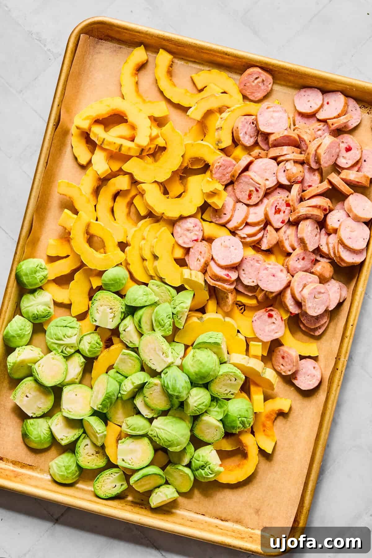 Sheet Pan Roasted Delicata Squash and Chicken Sausage 4 A sheet pan loaded with uncooked slices of chicken sausage, halved Brussels sprouts, and crescent-shaped delicata squash.