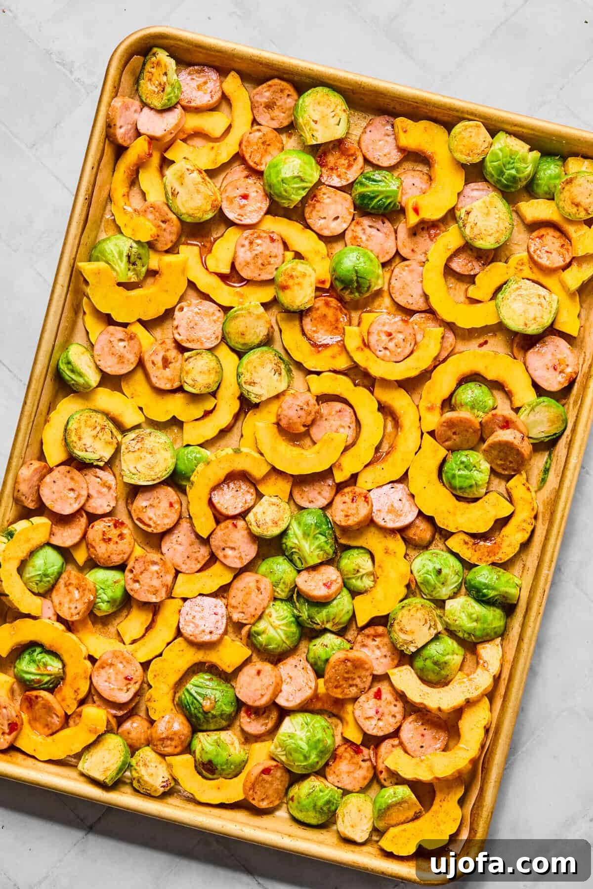 Sheet Pan Roasted Delicata Squash and Chicken Sausage 6 Veggies and sausage mixed thoroughly on a sheet pan, ensuring everything is evenly coated with the maple-spice mixture.