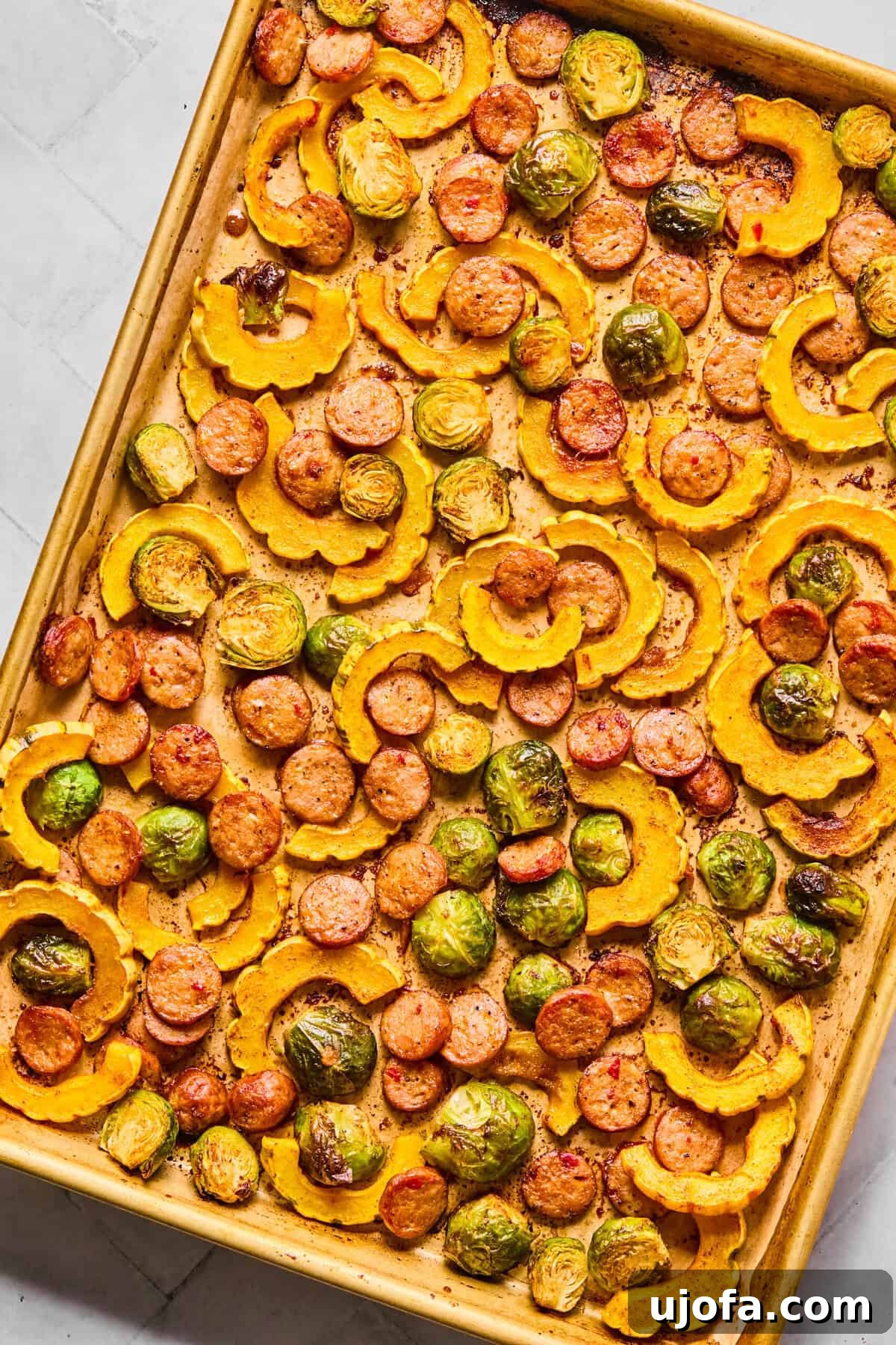 Sheet Pan Roasted Delicata Squash and Chicken Sausage 7 A sheet pan filled with golden-brown delicata squash, crispy Brussels sprouts, and browned chicken sausage, freshly roasted.