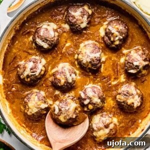 French onion meatballs in a skillet with a wooden spoon, ready to be served.