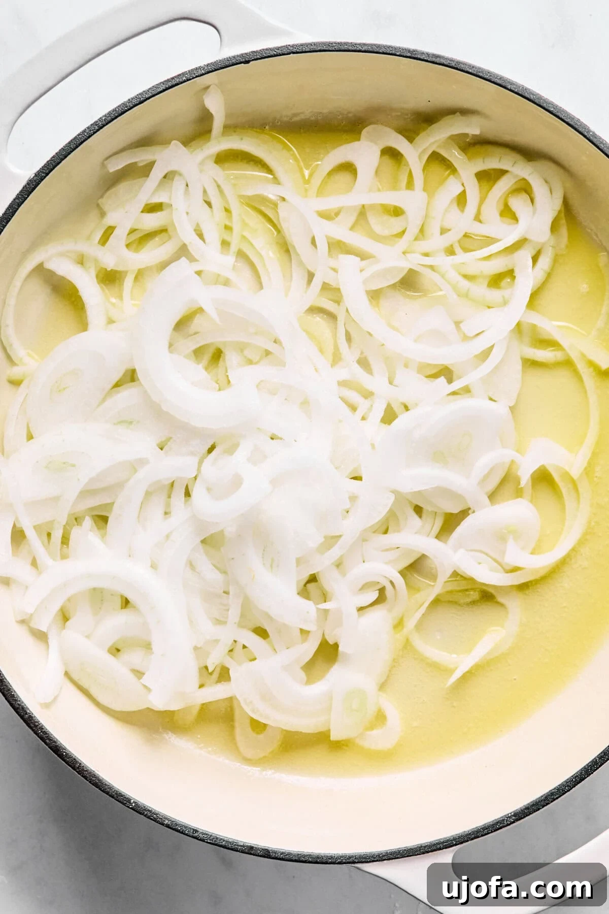 Savory French Onion Meatballs with Rich Gravy 4 Large oven-safe skillet with melted butter and thinly sliced yellow onions beginning to cook.
