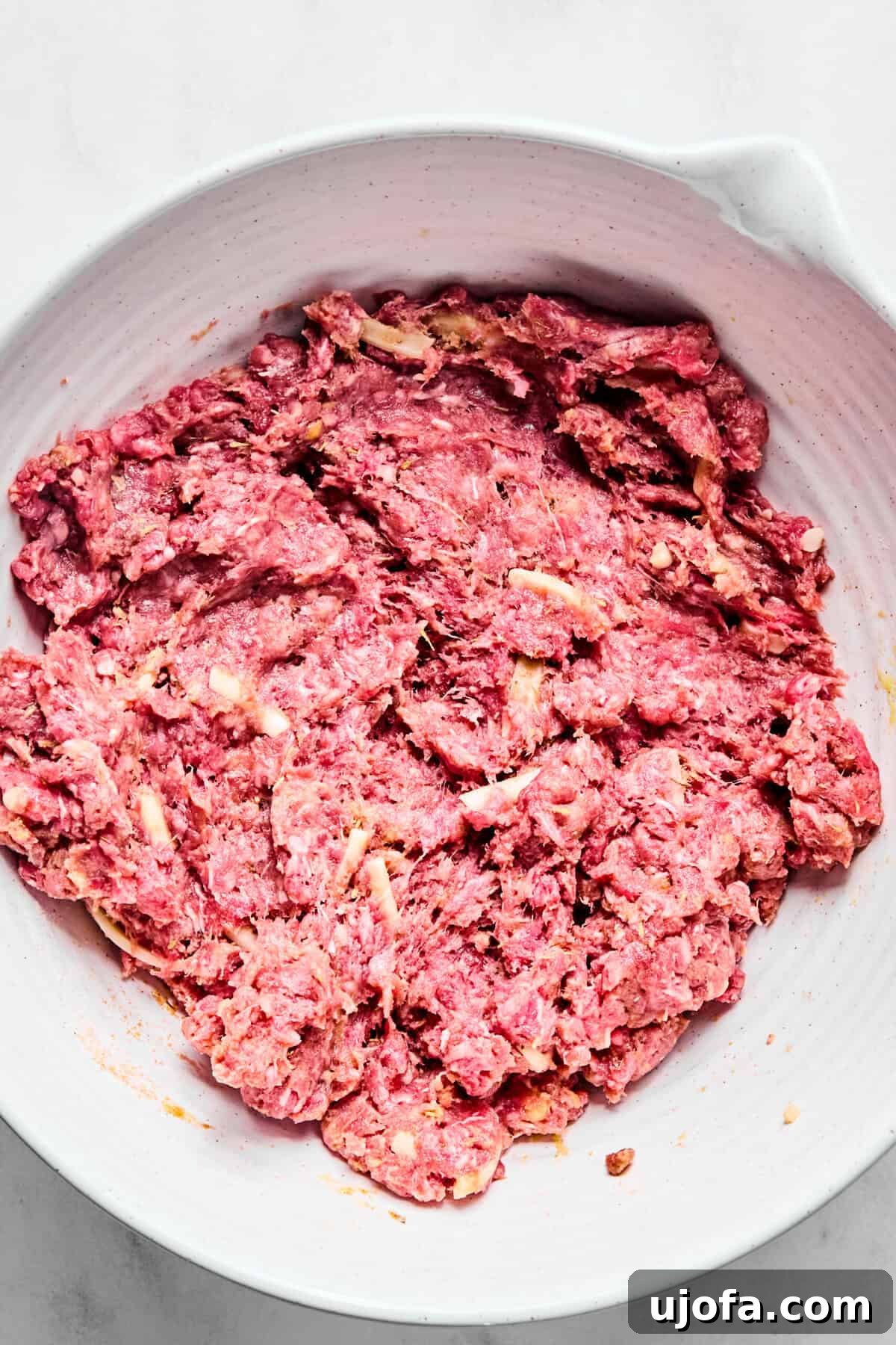 Savory French Onion Meatballs with Rich Gravy 6 A white bowl containing ground beef, gluten-free flour, an egg, various seasonings, Worcestershire sauce, and shredded cheese, ready to be mixed for meatballs.