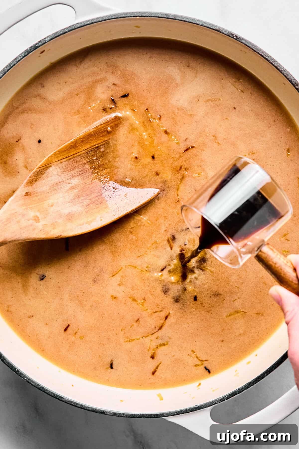 Savory French Onion Meatballs with Rich Gravy 9 Beef broth, Worcestershire sauce, dried thyme, and salt being poured into the oven-safe skillet, over the floured caramelized onions, with a whisk nearby.
