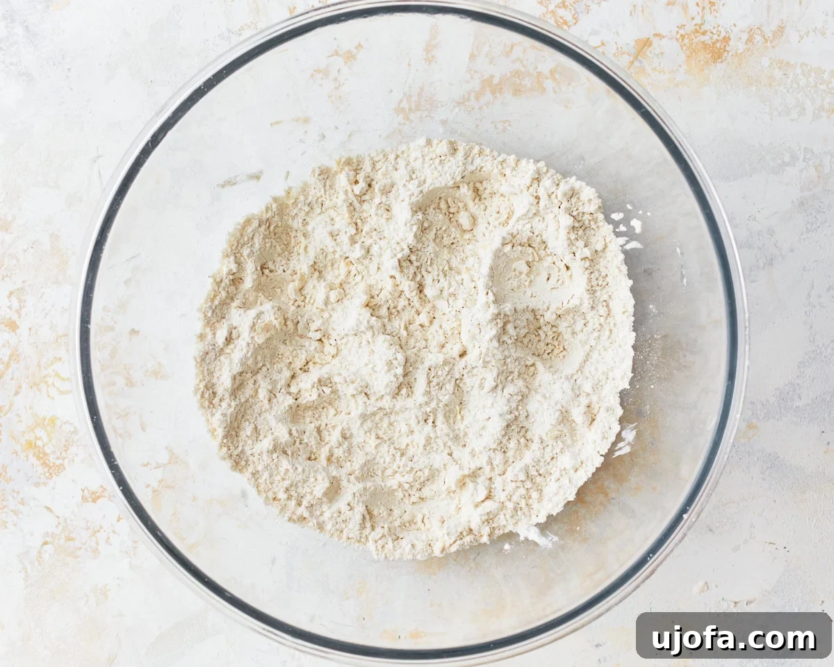 Cubed cold butter being cut into the dry ingredients for gluten-free puff pastry within a glass mixing bowl using a pastry cutter.