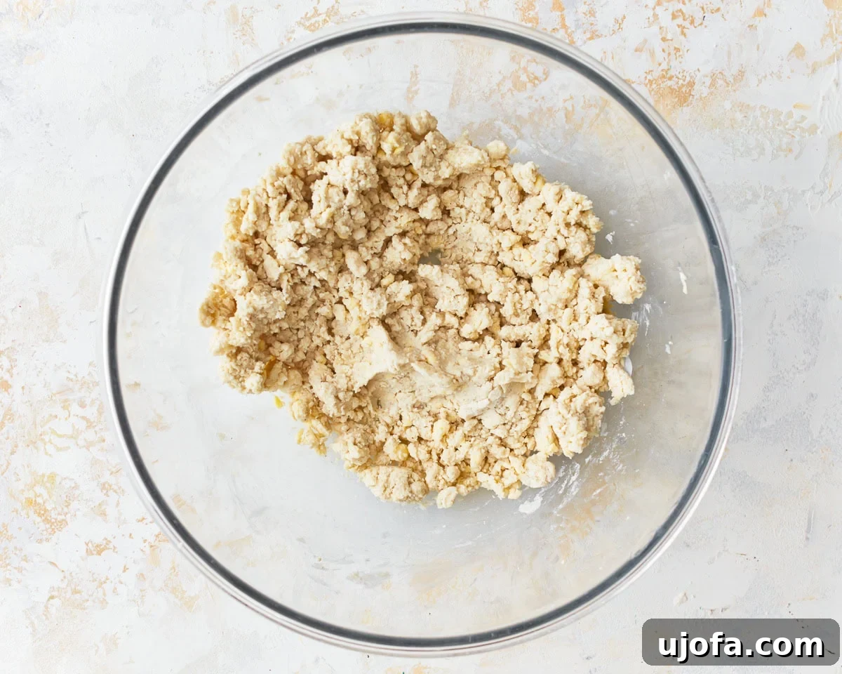 A loose, shaggy dough forming in a glass mixing bowl after cold water has been added to the gluten-free puff pastry mixture.