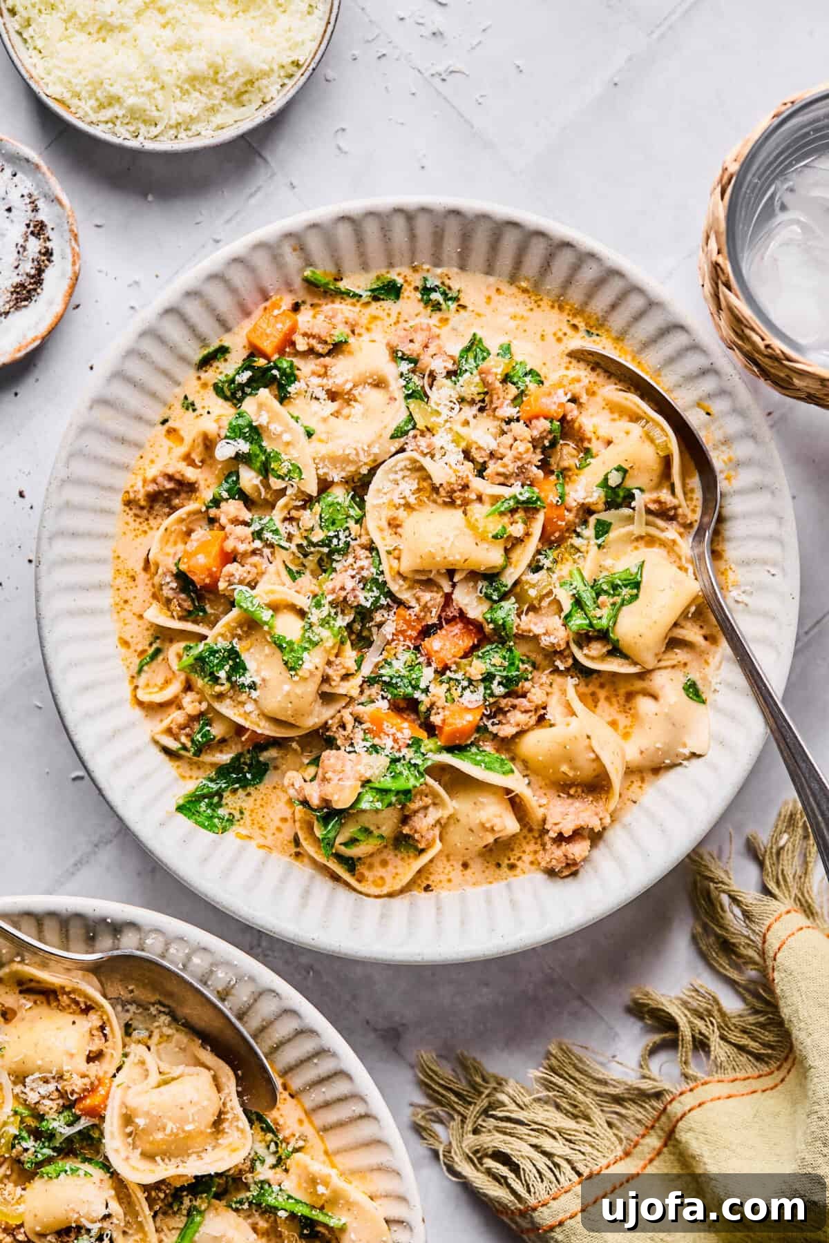 A hearty bowl of creamy sausage tortellini soup, garnished with fresh spinach and vibrant vegetables, with a hint of a rich boursin cheese sauce.