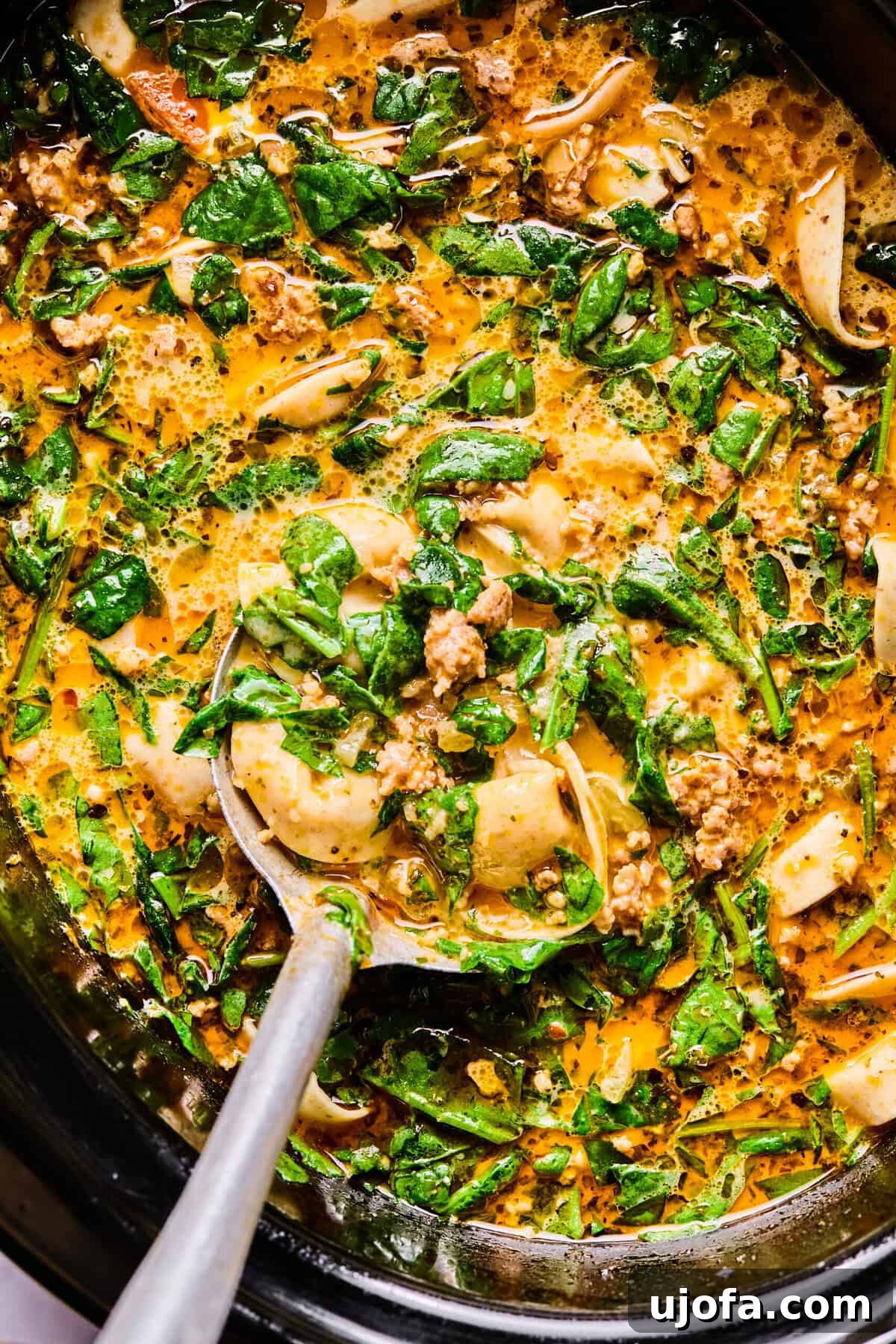 The finished slow cooker Italian sausage and tortellini soup, creamy and delicious, served directly from the pot with a large silver spoon.