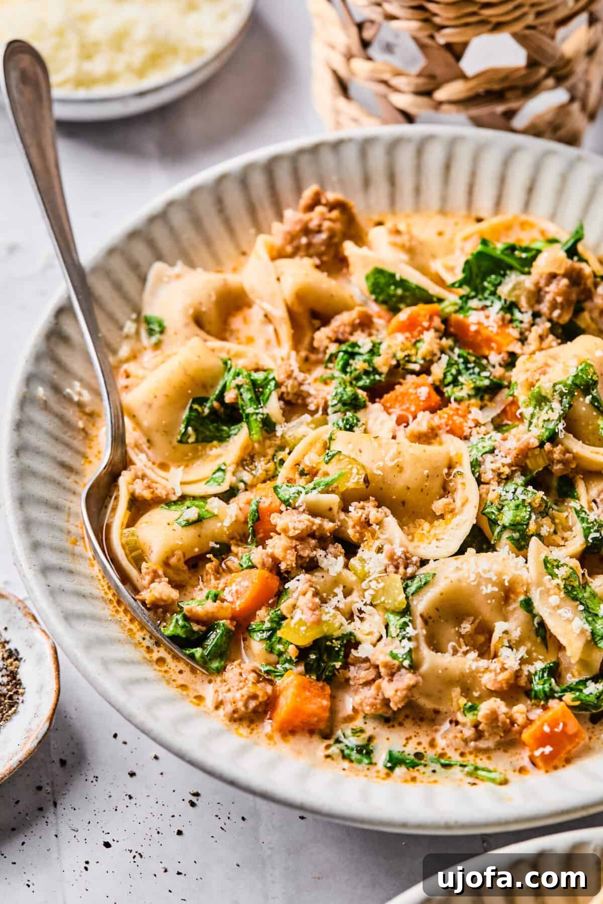 A close-up view of the rich and creamy sausage tortellini soup, topped with fresh spinach, vibrant vegetables, and a generous sprinkle of Parmesan cheese.