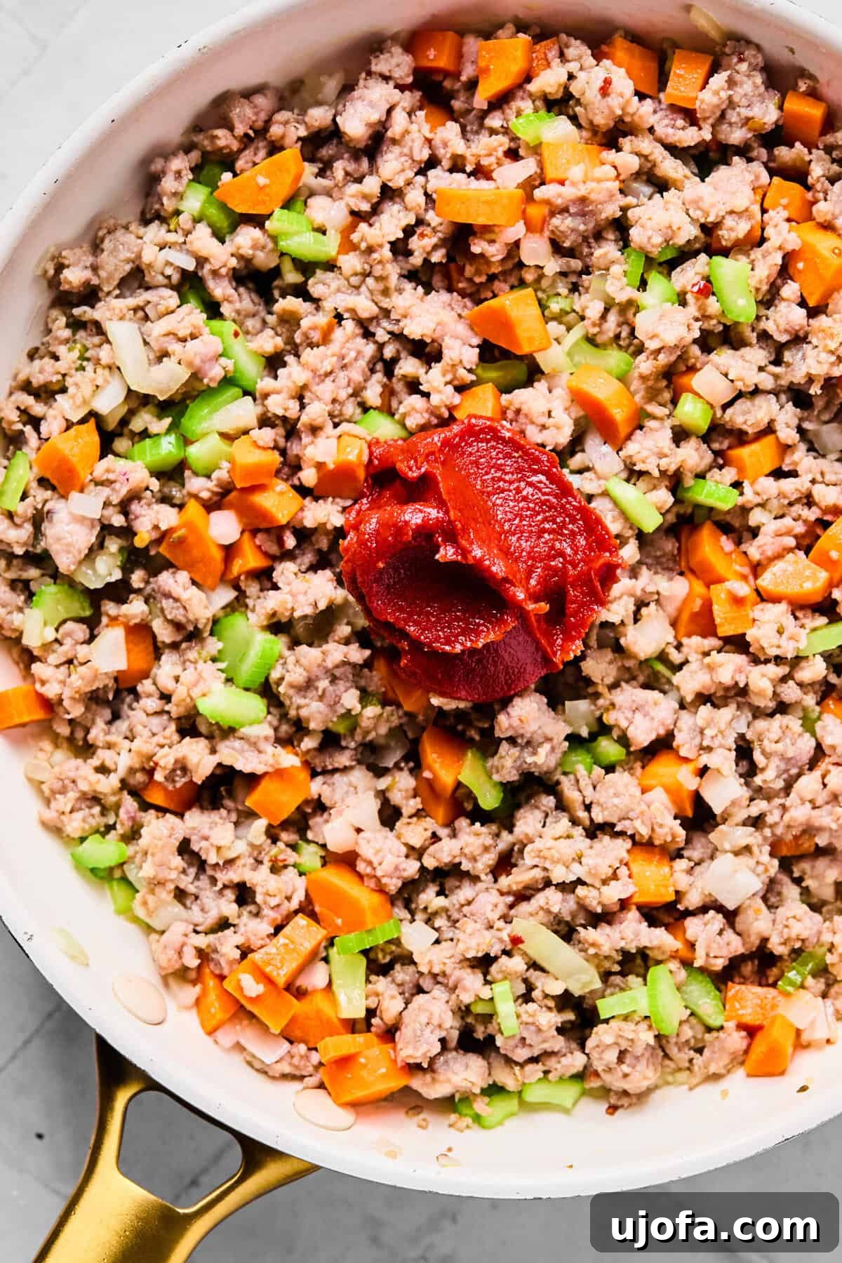 Sautéing diced onions, celery, carrots, and minced garlic with tomato paste in the skillet after browning the sausage.