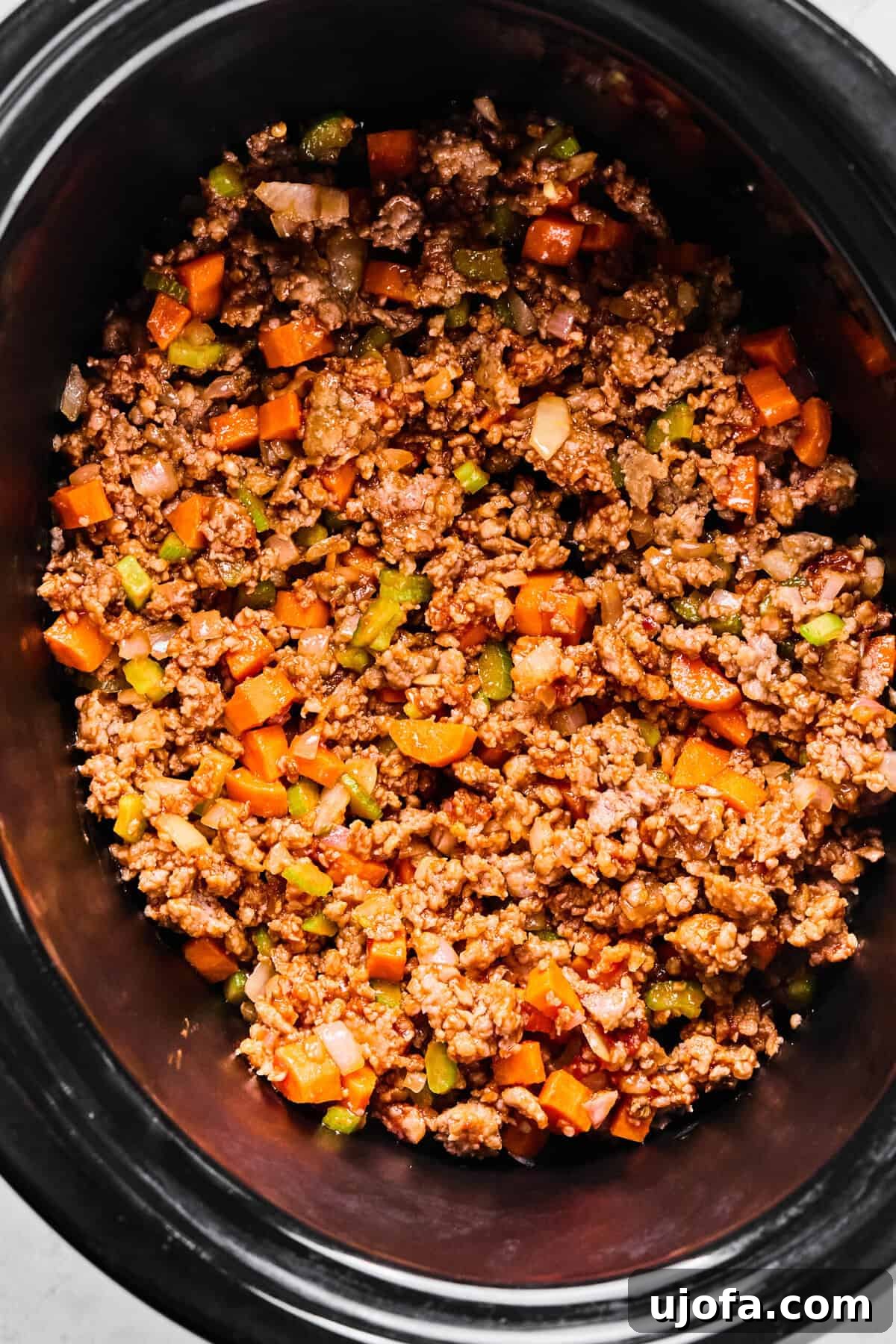 All sautéed ingredients, including browned sausage and vegetables, transferred into the slow cooker pot.