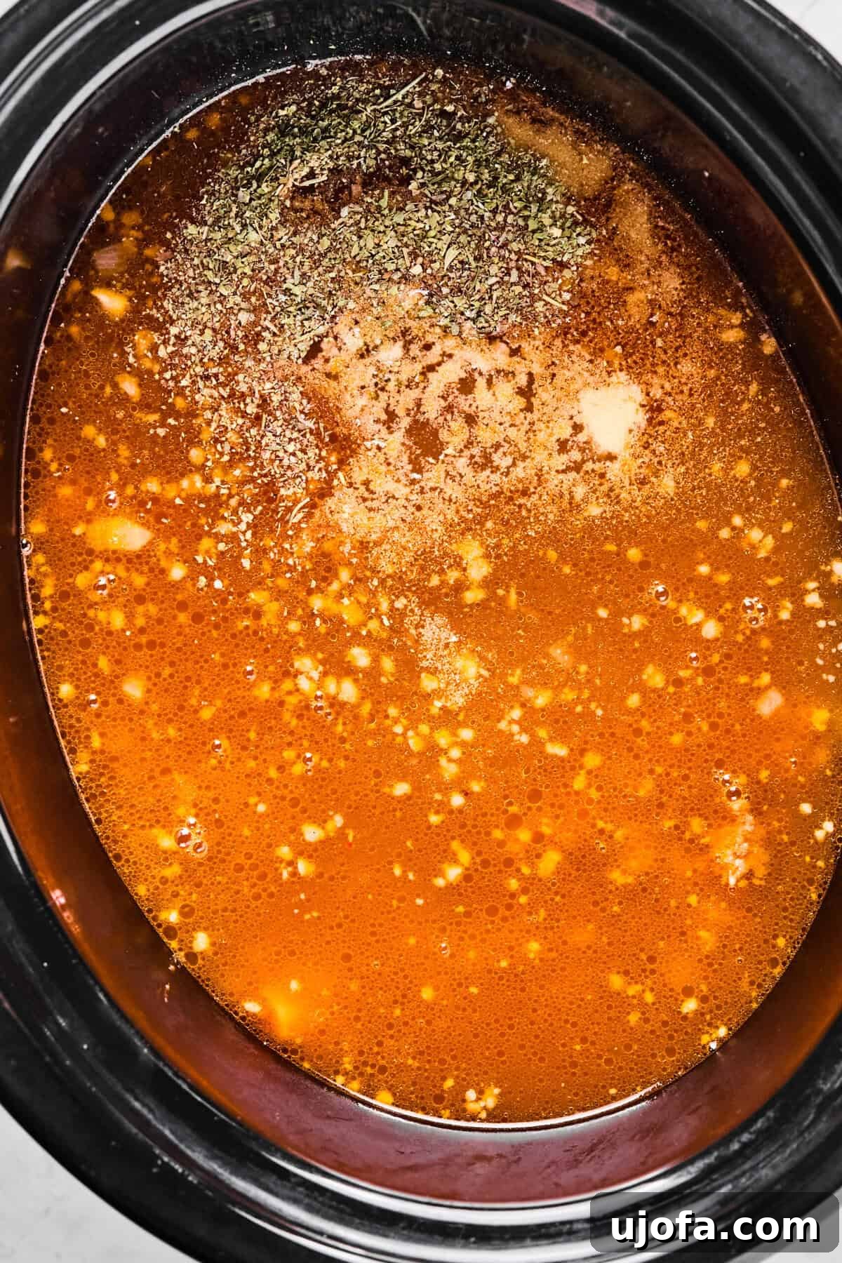 Chicken broth and a blend of seasonings poured over the sausage and vegetables in the slow cooker, ready for simmering.