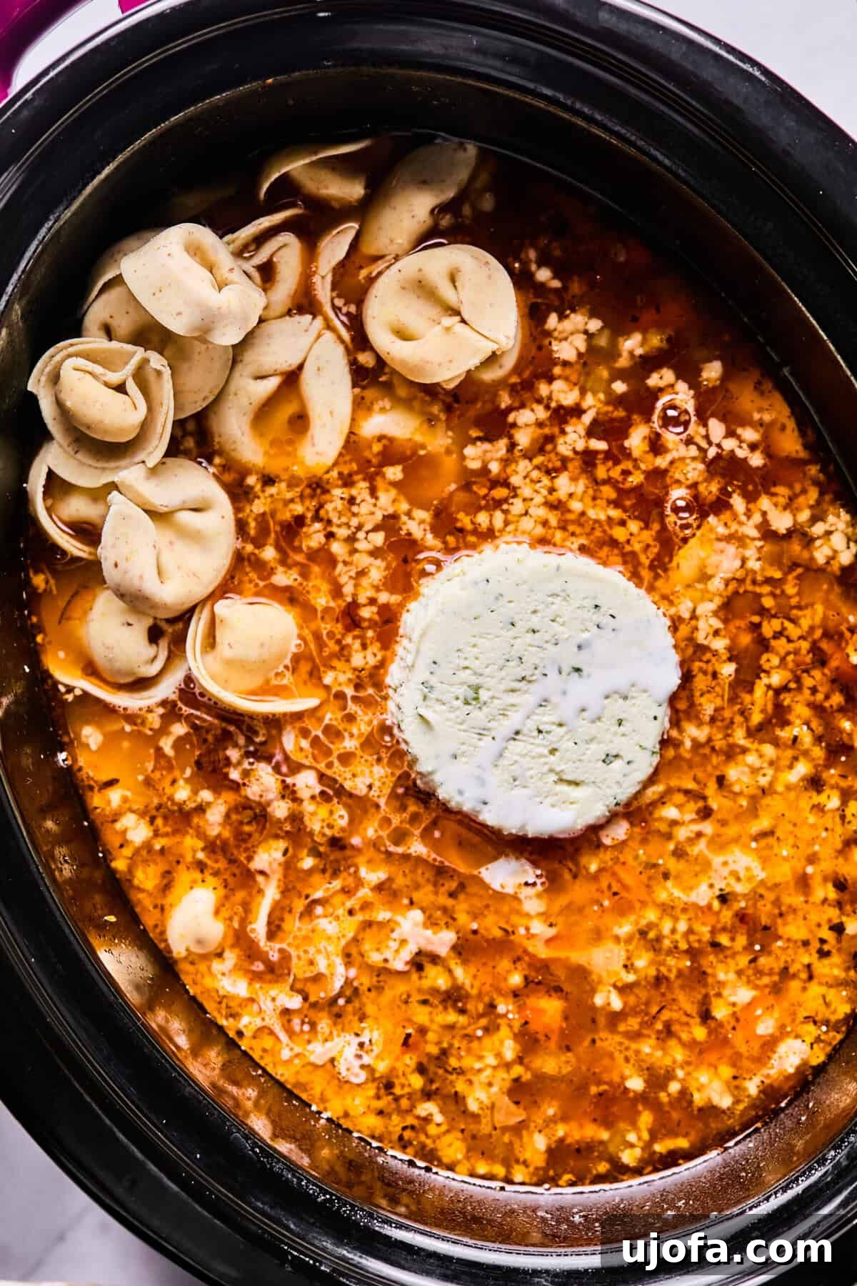 Adding gluten-free tortellini, Boursin cheese, and half and half to the slow cooker soup, stirring to combine.