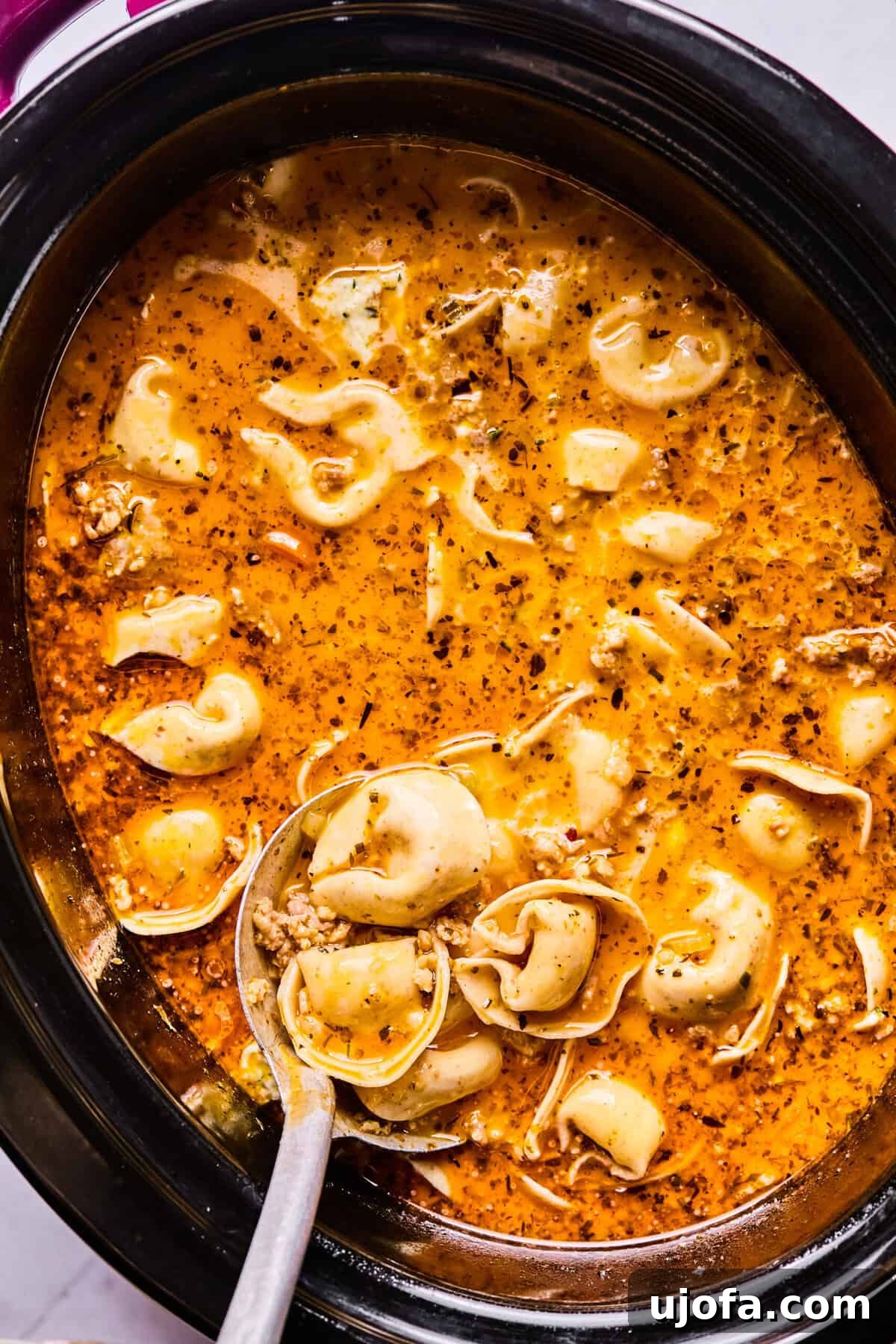 Perfectly cooked tortellini resting in the creamy sausage soup within the slow cooker, ready for the final touches.