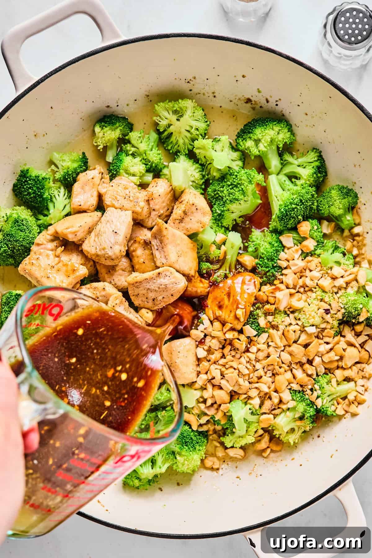 Speedy Chicken and Broccoli Stir-Fry 7 Chicken and cashews added back to large sauté pan with broccoli; stir fry sauce is being poured in.