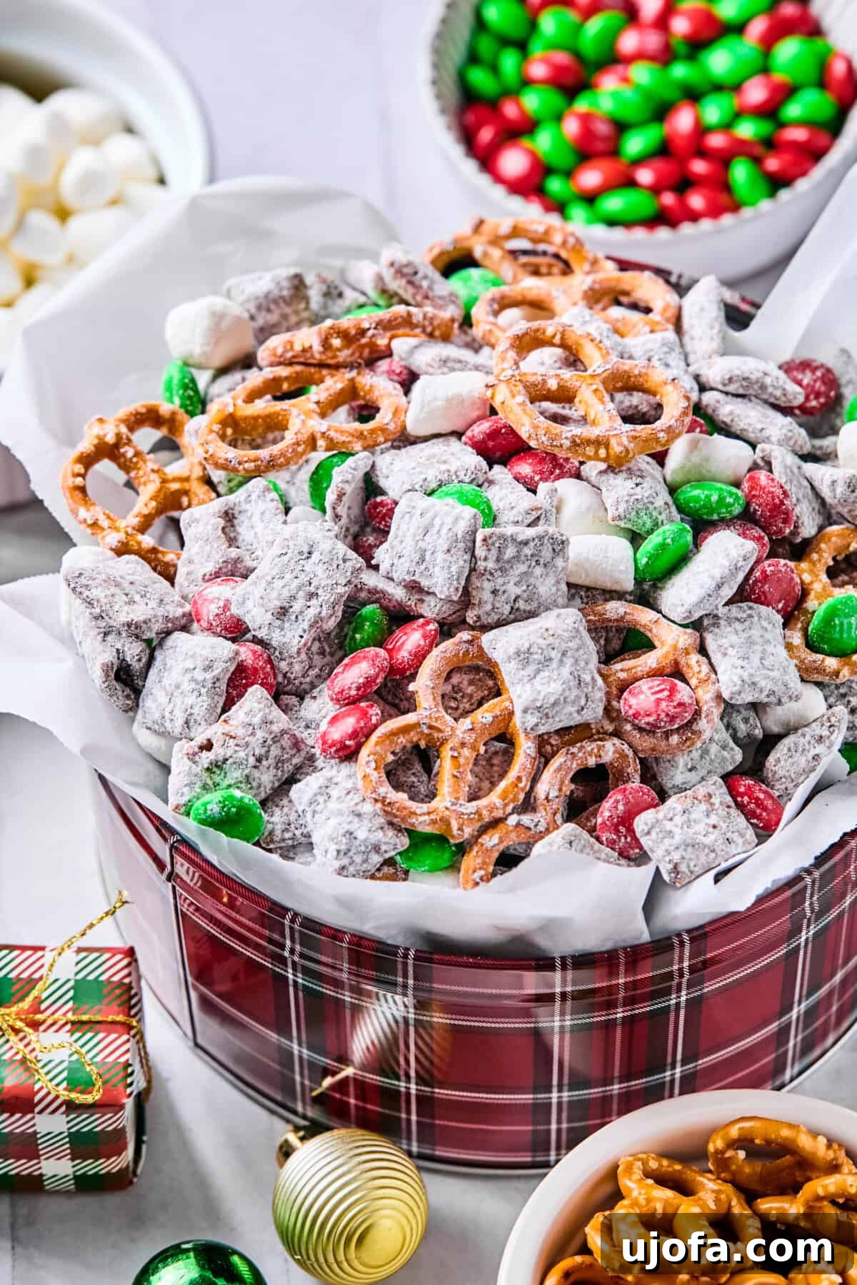 A festive parchment-lined tin filled with Christmas puppy chow on a white countertop.