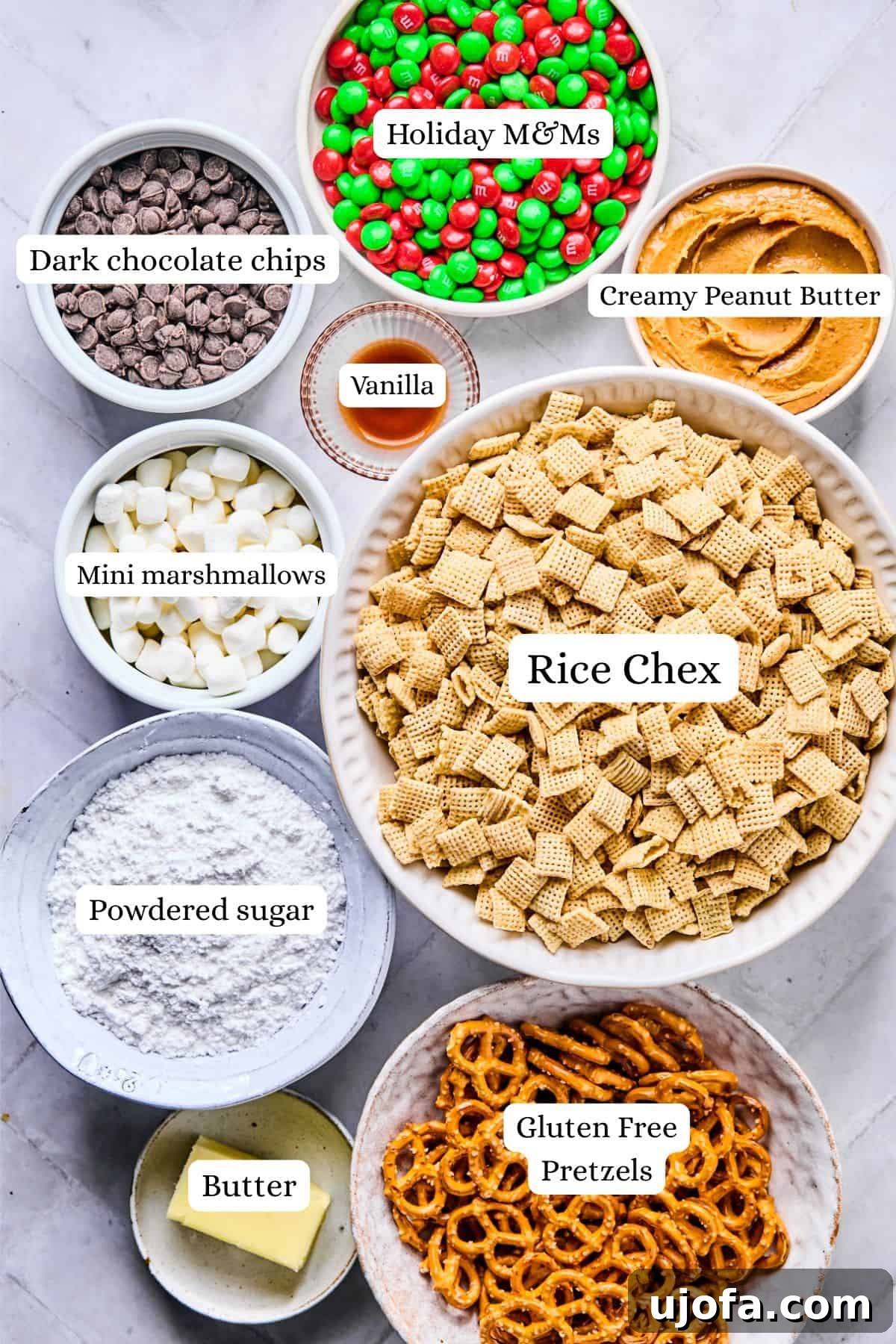 Christmas puppy chow ingredients labeled and laid out in bowls including rice chex, powdered sugar, pretzels, peanut butter, vanilla, and chocolate chips.