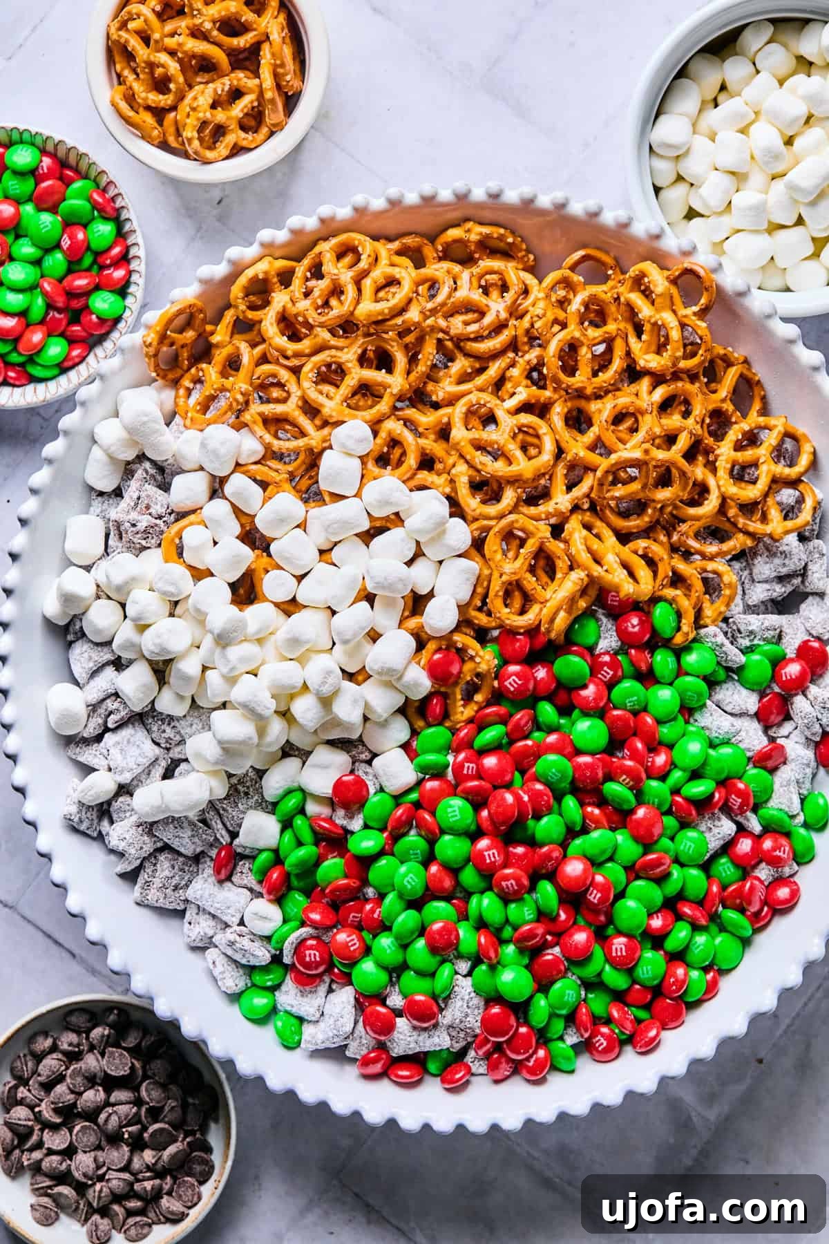 Cereal mixture in a clean bowl with gluten-free pretzels, Christmas M&Ms, and marshmallows; ready to combine.