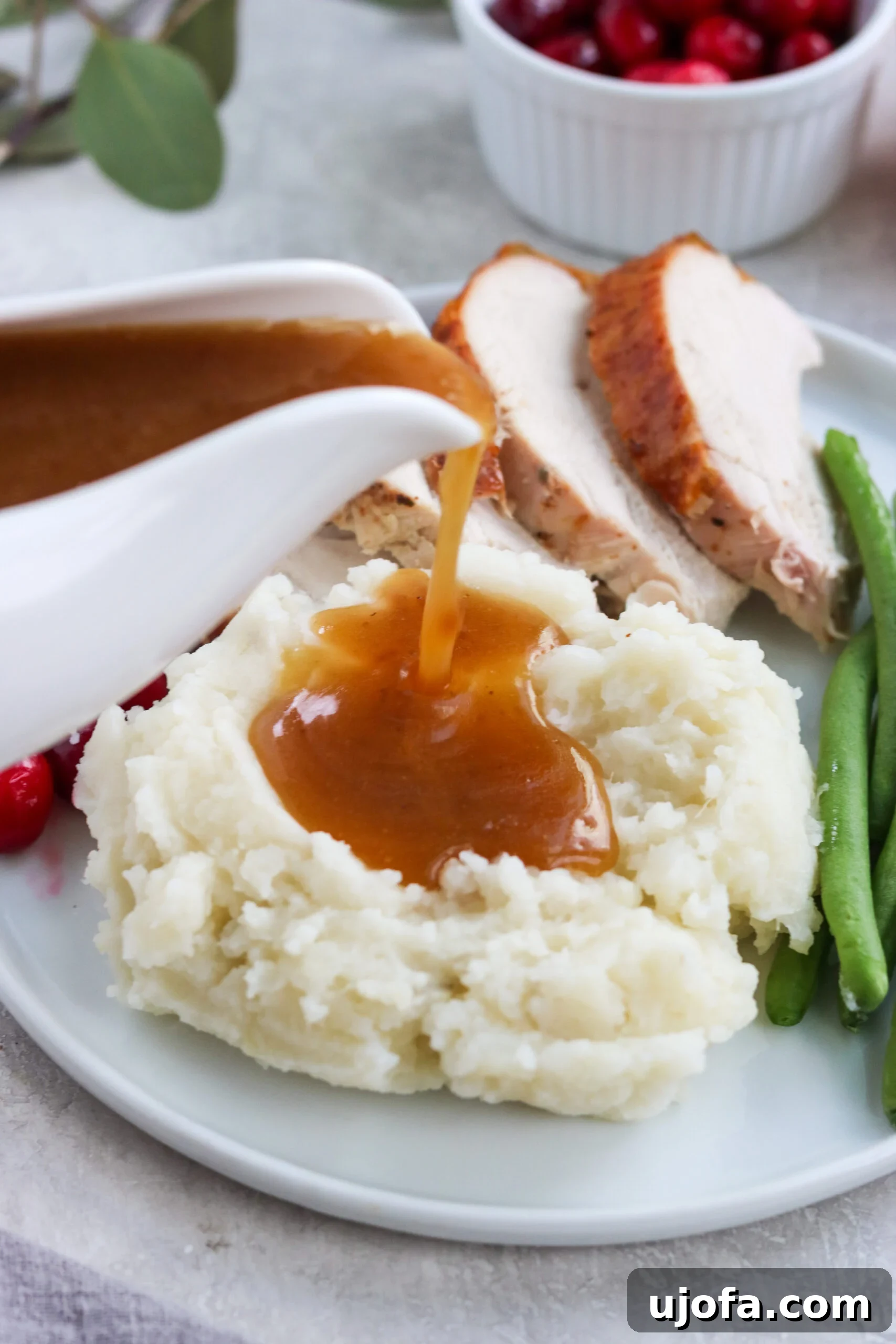 Buttery Smooth Dairy-Free Mash 6 paleo gravy being poured on mashed potatoes with roasted turkey in the background