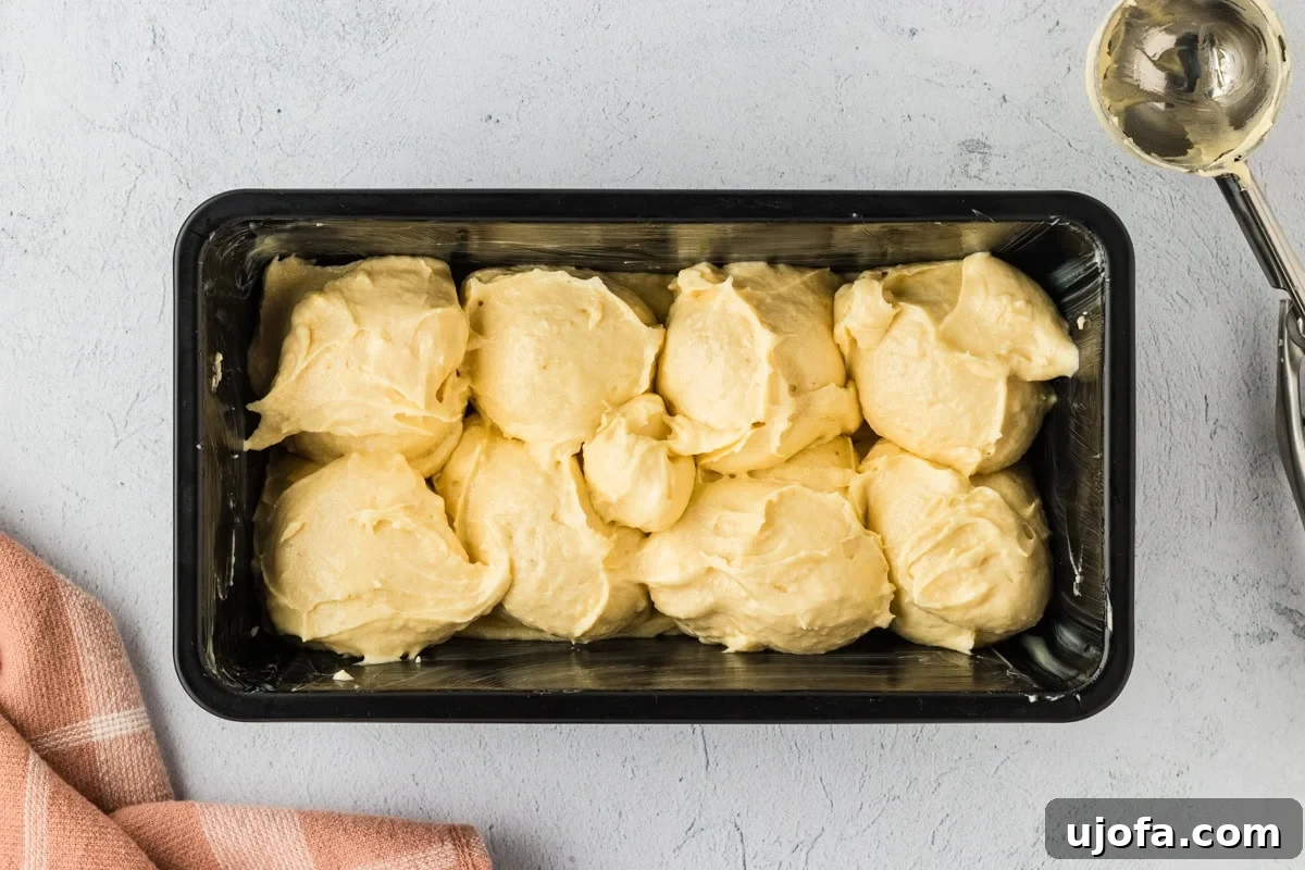 Gluten-free brioche batter carefully dolloped into a loaf pan using a cookie scoop, creating signature peaks and valleys.
