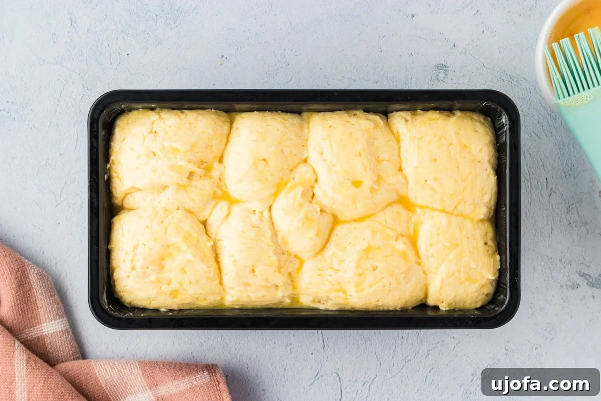 Gluten-free brioche dough in a loaf pan, brushed with an egg wash just before baking to ensure a golden crust.