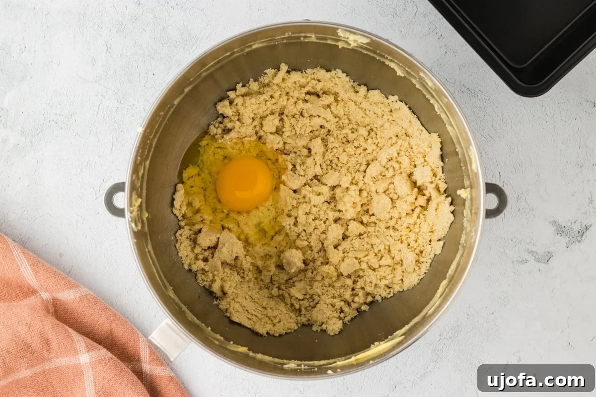 Softened butter and eggs being added sequentially to the dry ingredients in a stand mixer bowl for gluten-free brioche.